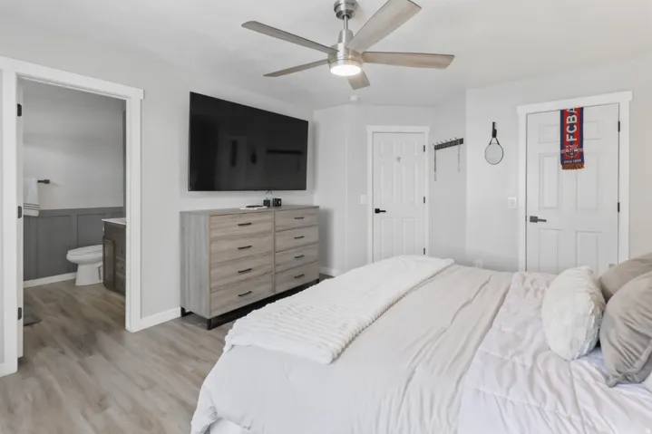 Bedroom with light wood-type flooring, a ceiling fan, a wainscoted wall, and connected bathroom