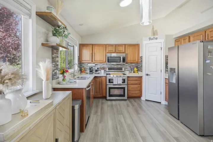 Kitchen with stainless steel appliances, open shelves, vaulted ceiling, light wood-style flooring, and wood finish cabinets