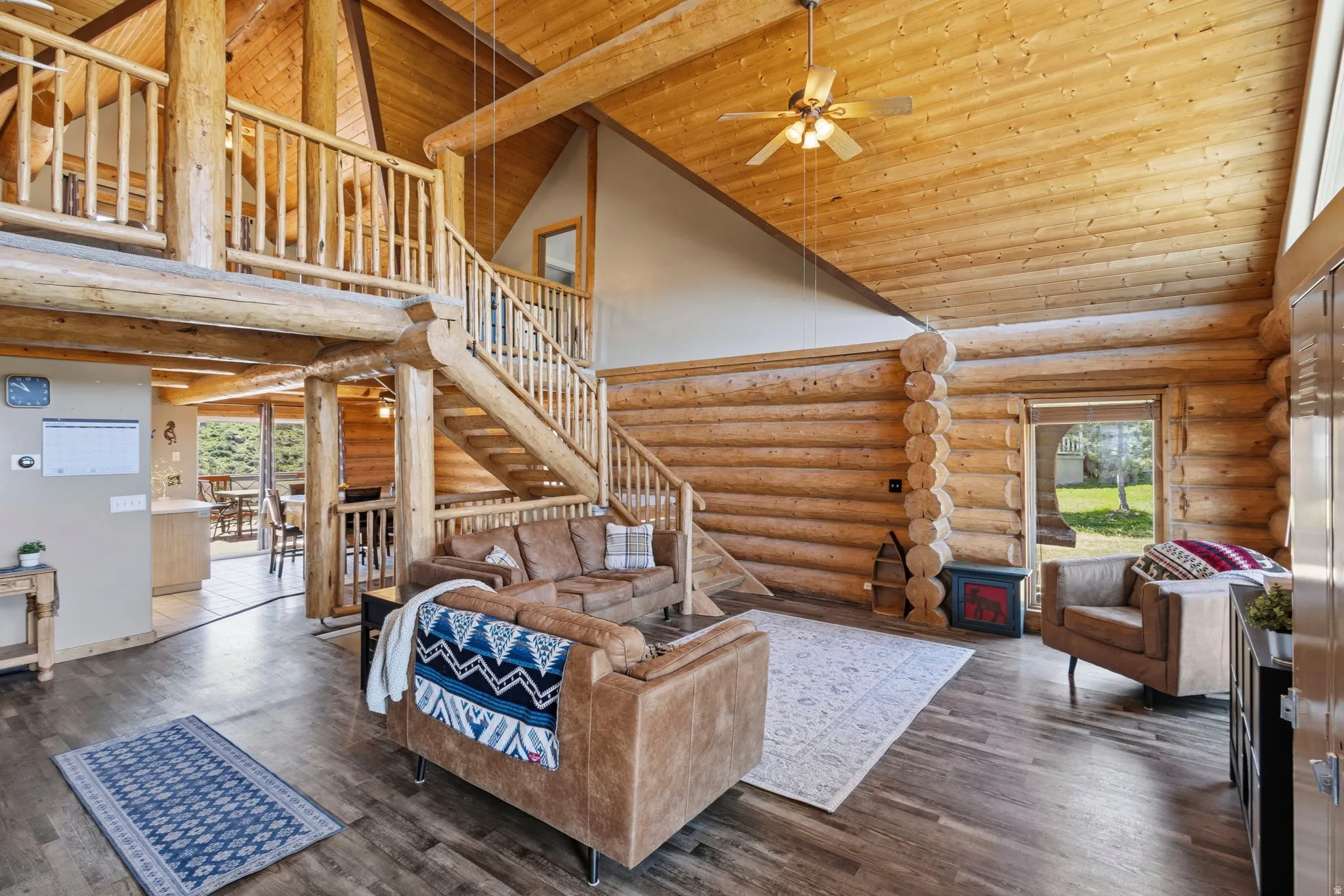 Living room featuring a vaulted wood ceiling, log walls, a ceiling fan, and dark wood-style flooring