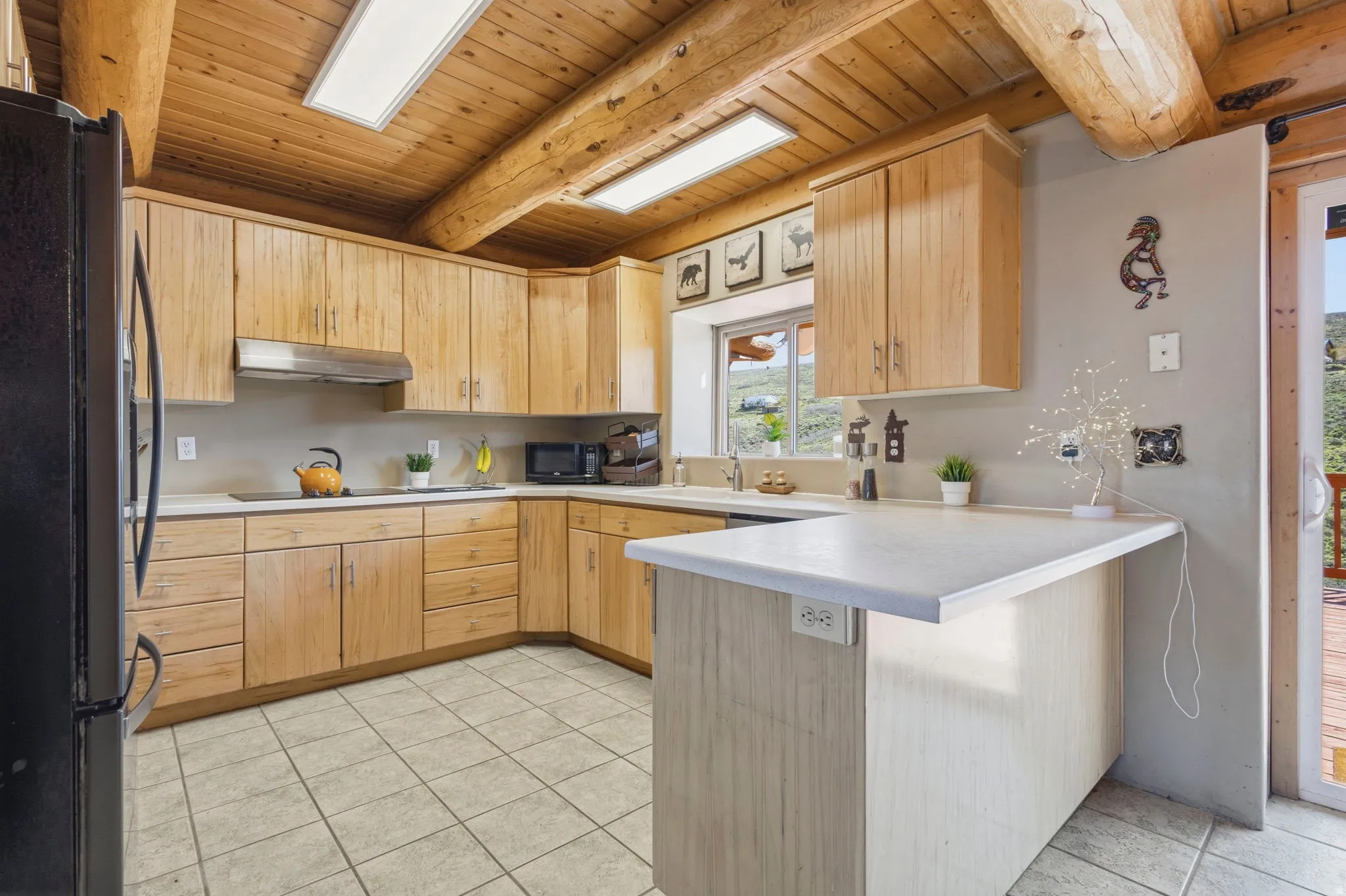 Kitchen with black appliances, light wood finish cabinets, a peninsula, light countertops, and a wooden ceiling with exposed beams
