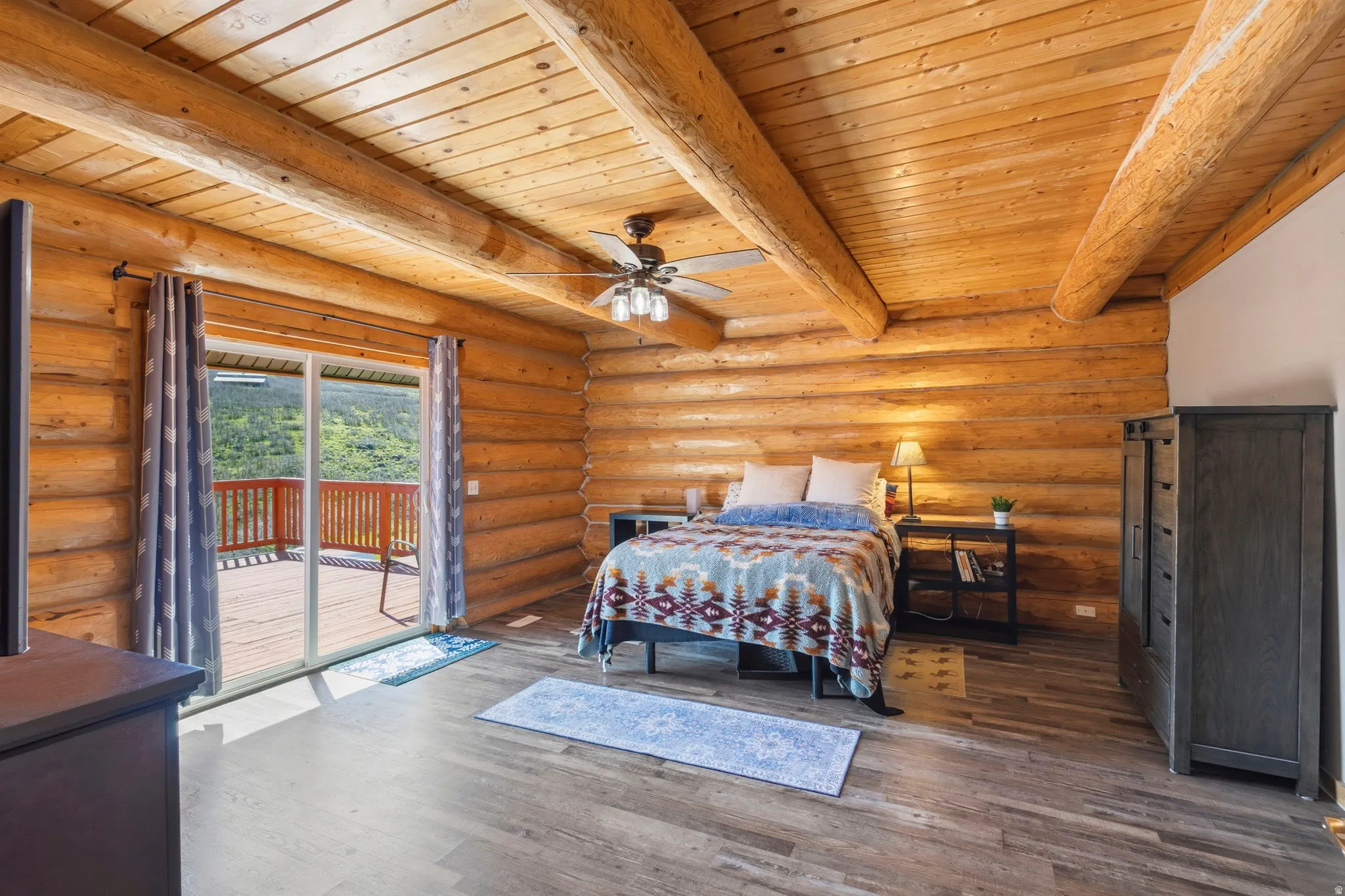 Bedroom featuring rustic walls, wood finished floors, a wooden ceiling with exposed beams, access to exterior, and a ceiling fan