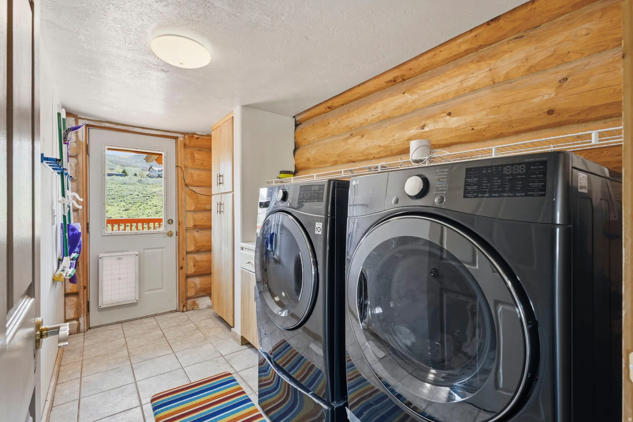 Laundry room featuring rustic walls, a textured ceiling, washer and clothes dryer, light tile patterned flooring, and heating unit