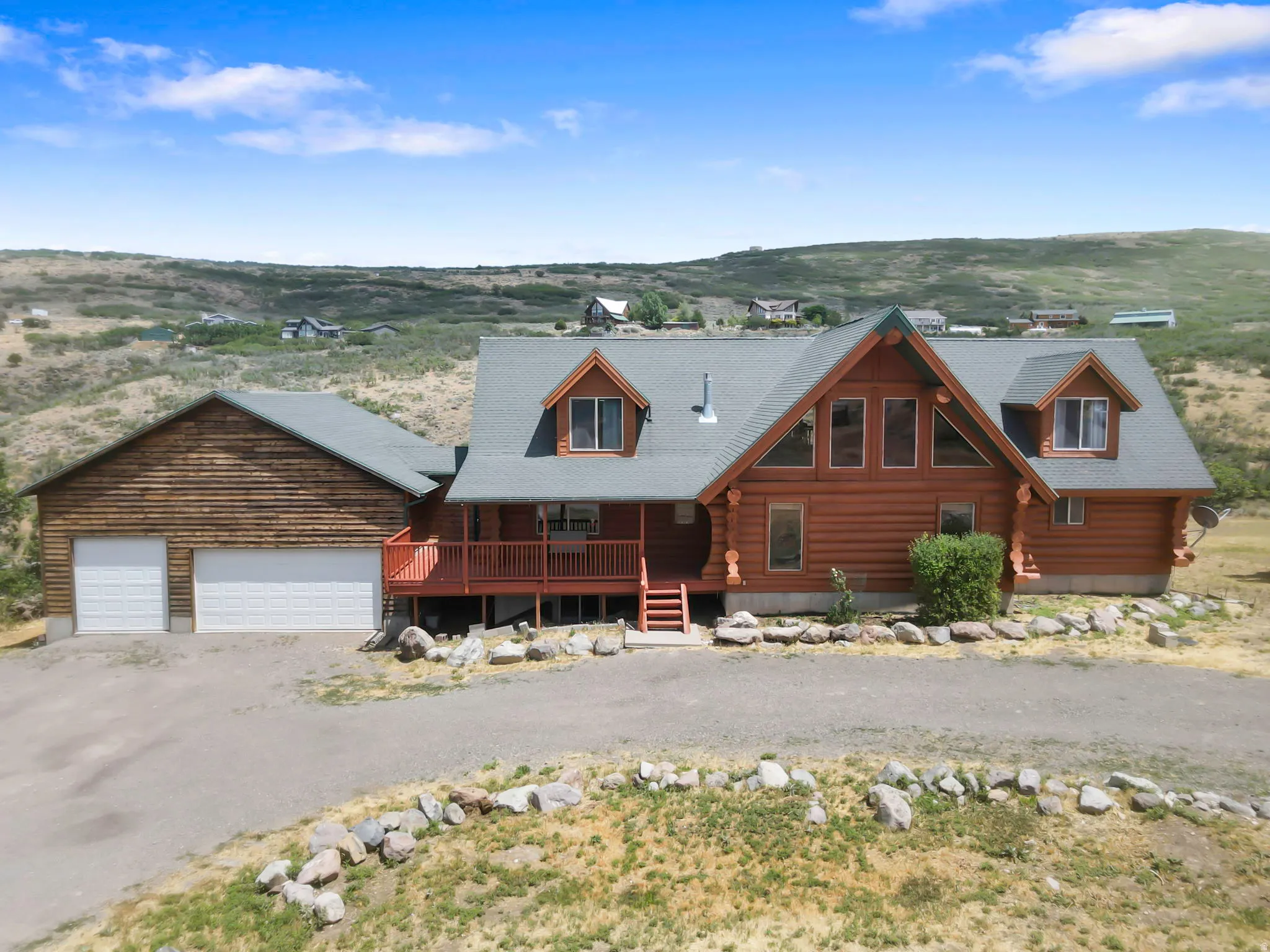 Log cabin residence featuring a red-stained exterior, an attached two-car garage, multiple dormer windows, and a covered porch with red railings