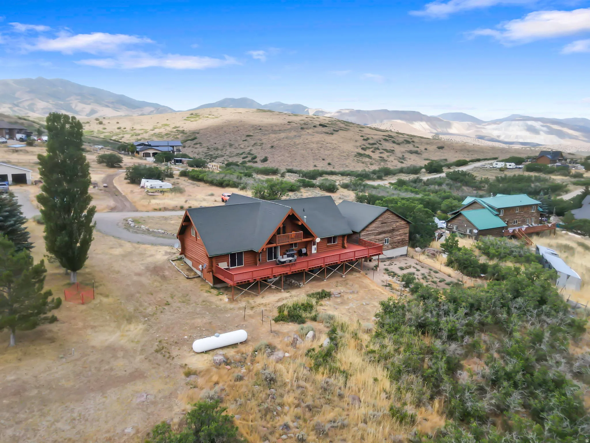 Log-style residence featuring an expansive red-stained deck, dark shingle roof, and a prominent propane tank