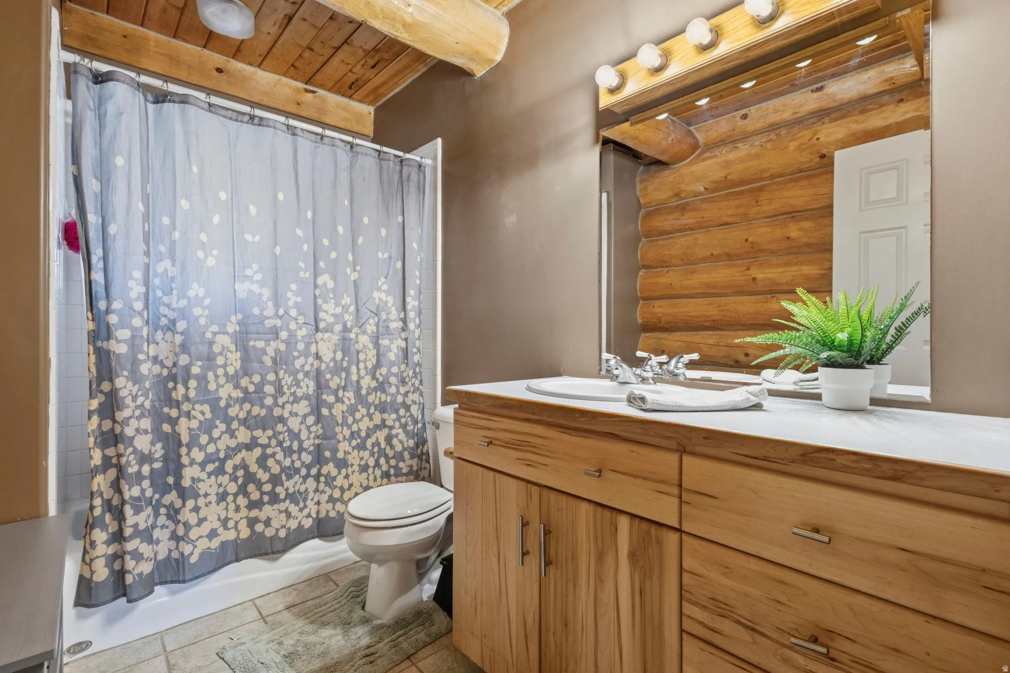 Bathroom featuring vanity, shower / tub combo with curtain, a wood ceiling with exposed beams, rustic walls, and light tile patterned floors