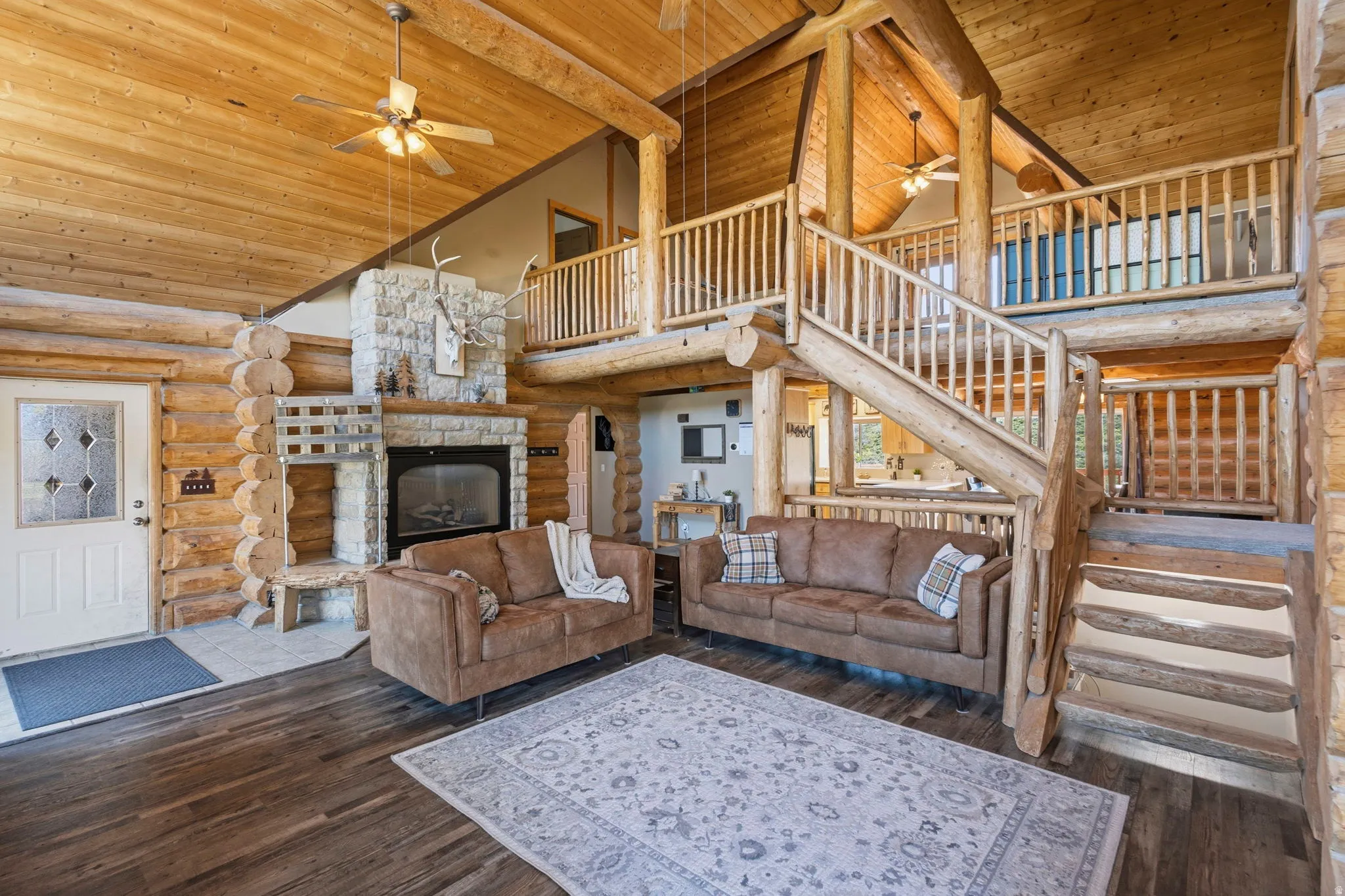 Living area with log walls, a high wood beamed ceiling, ceiling fan, dark wood finished floors, and a stone fireplace