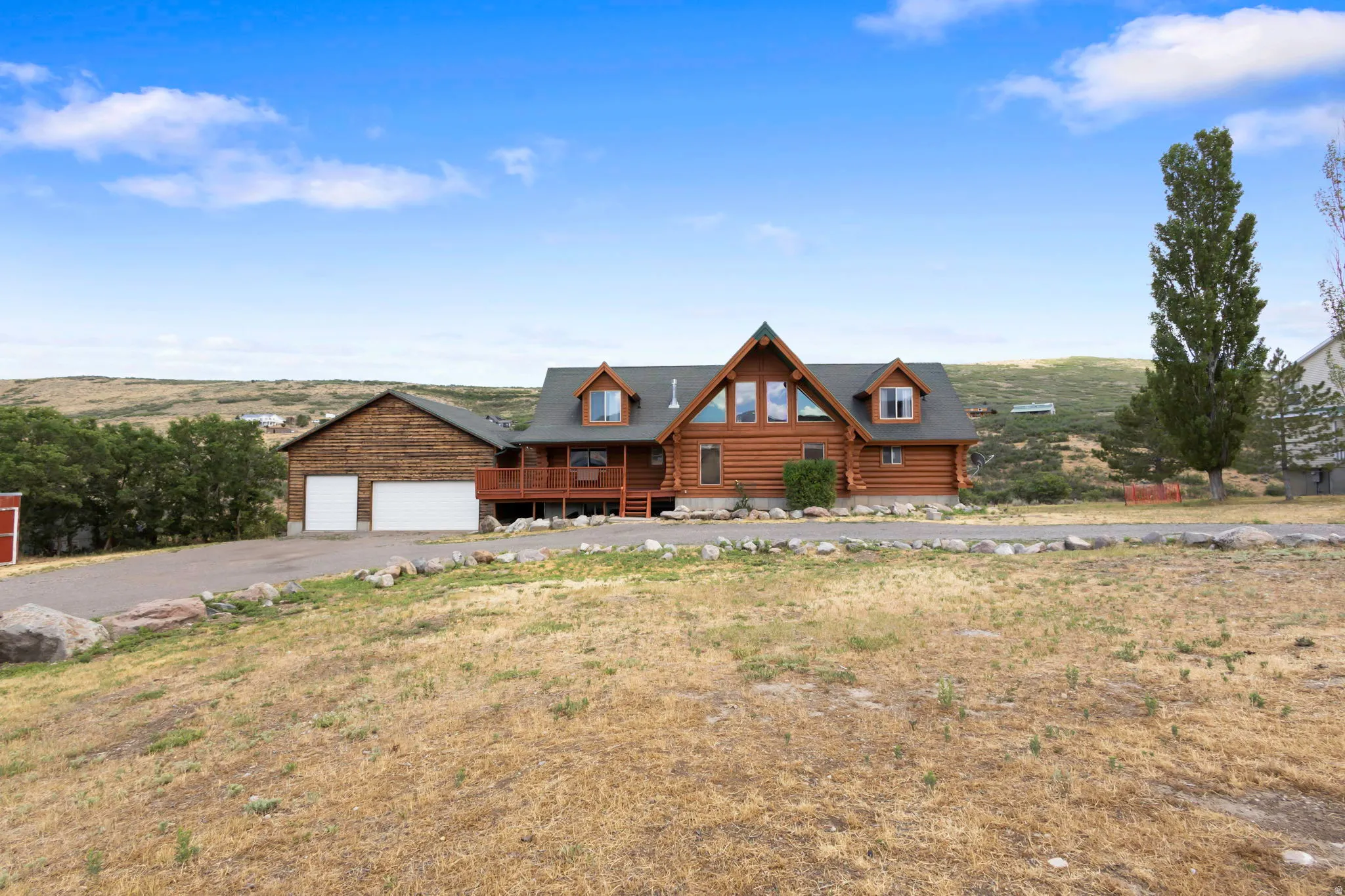 Log cabin style residence featuring a front deck, multiple dormer windows, and an attached two-car garage