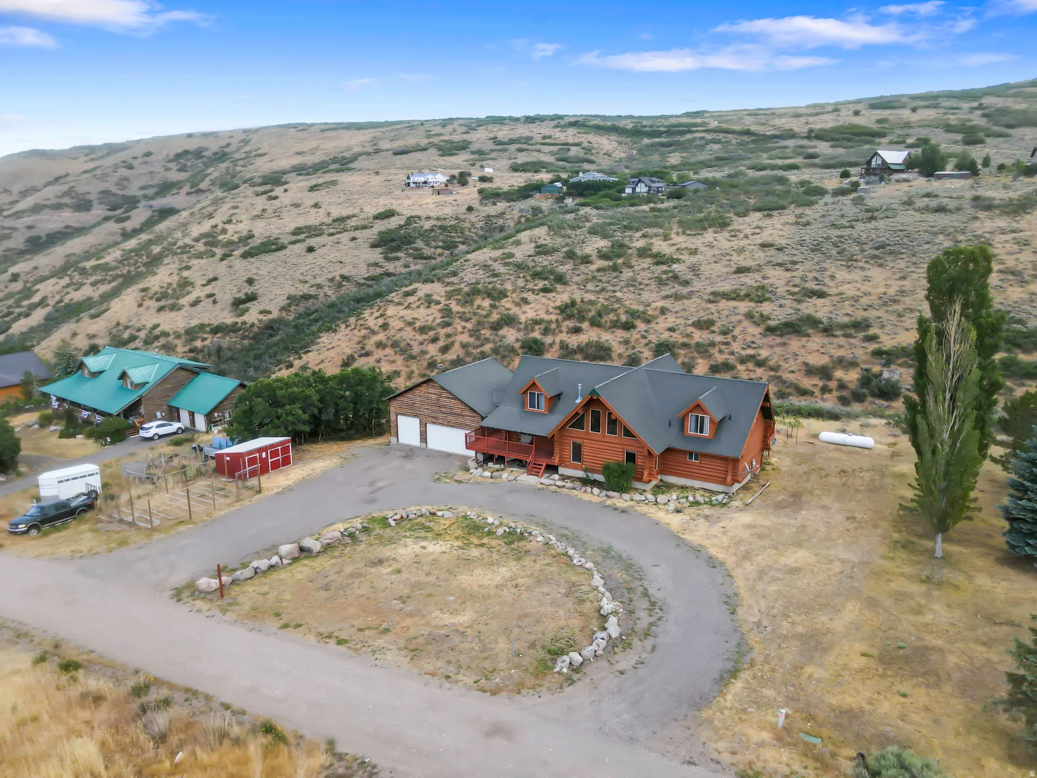 Log home exterior with a multi-car garage, dormer windows, and a surrounding natural landscape