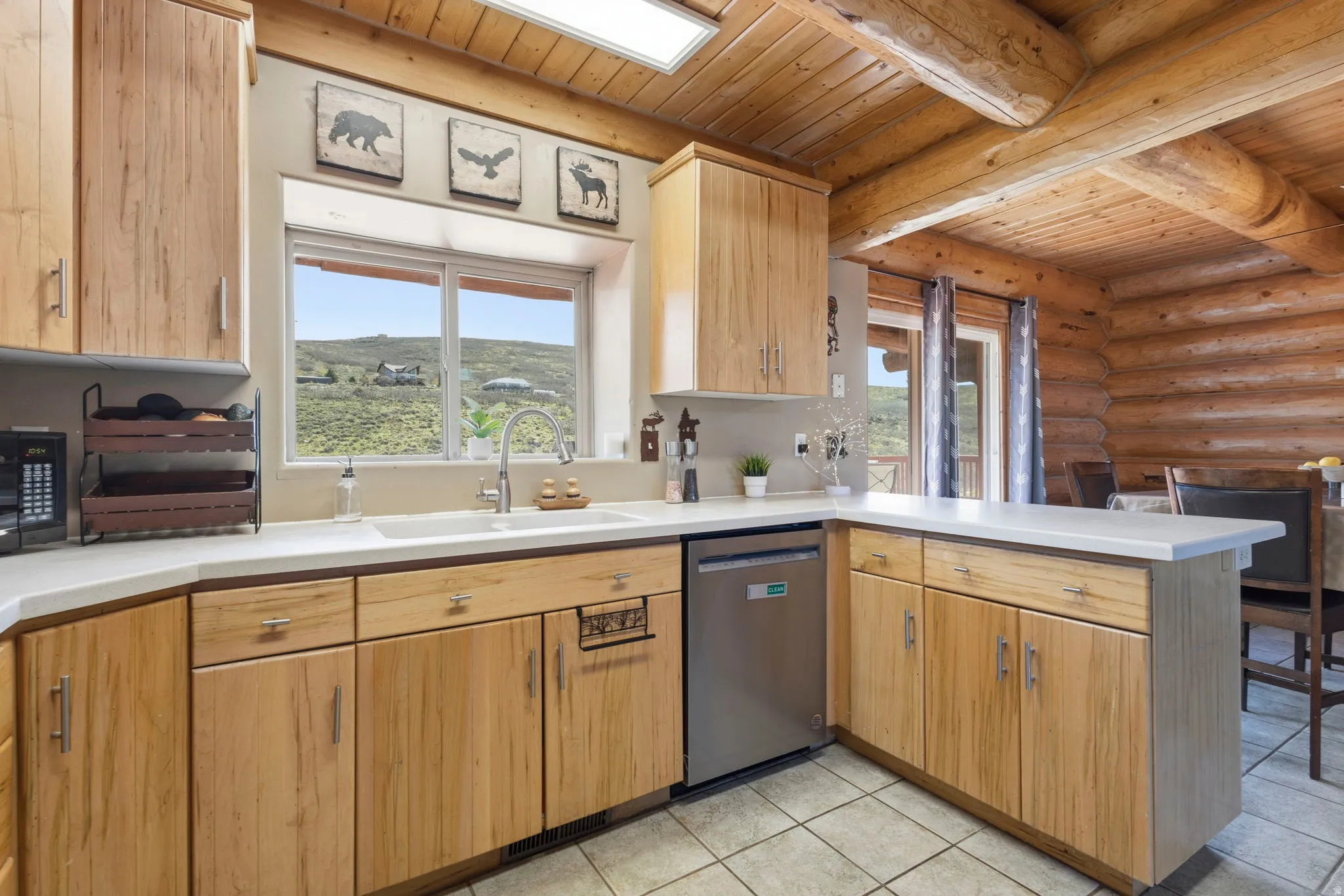 Kitchen featuring a peninsula, log walls, light countertops, stainless steel dishwasher, and a wood ceiling with exposed beams