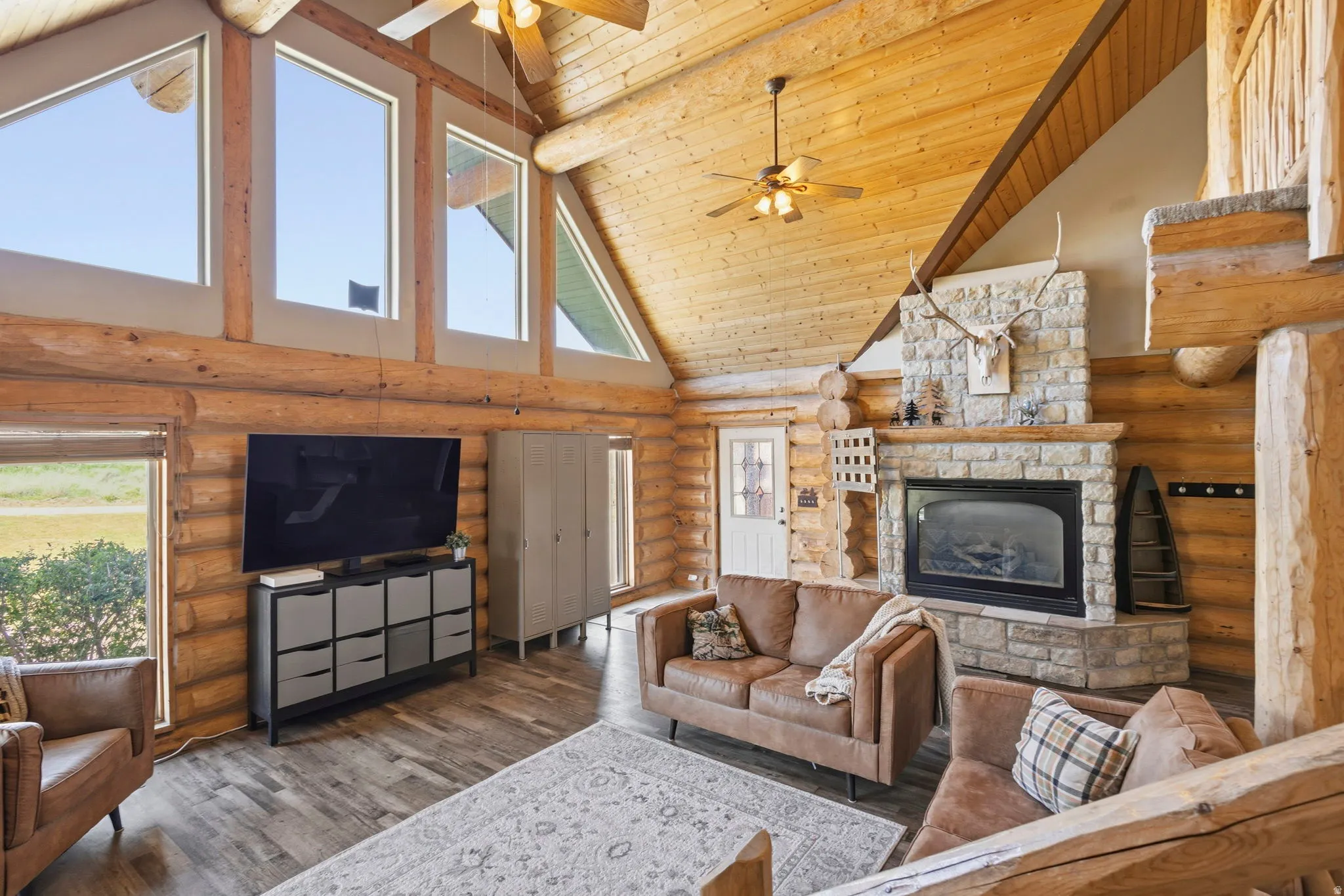 Living room featuring a stone fireplace, a high wood beamed ceiling, hardwood / wood-style floors, ceiling fan, and rustic walls