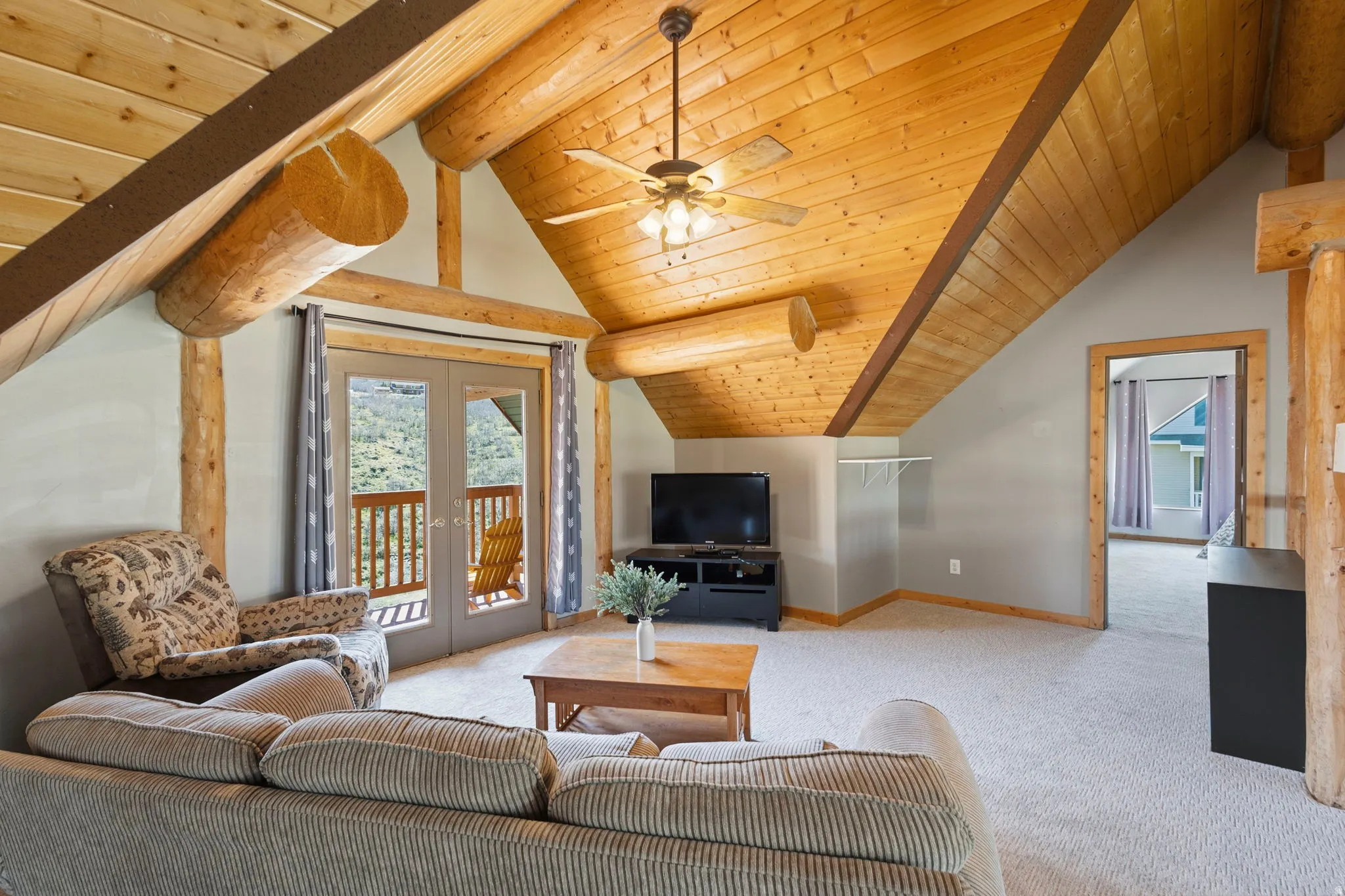 Living area featuring french doors, light carpet, ceiling fan, and a wood ceiling with exposed beams