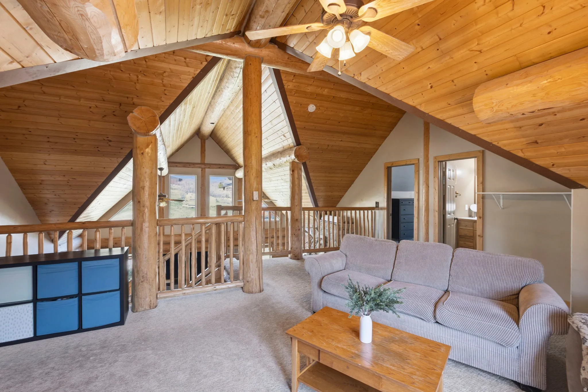 Living area with a ceiling fan, carpet floors, and a wood ceiling with exposed beams