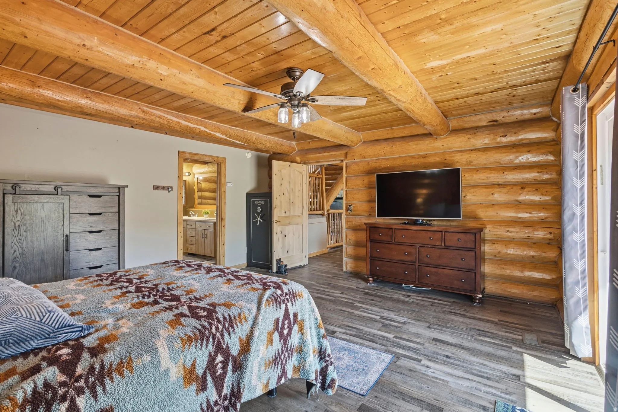 Bedroom with log walls, ensuite bath, a wood ceiling with exposed beams, wood finished floors, and ceiling fan