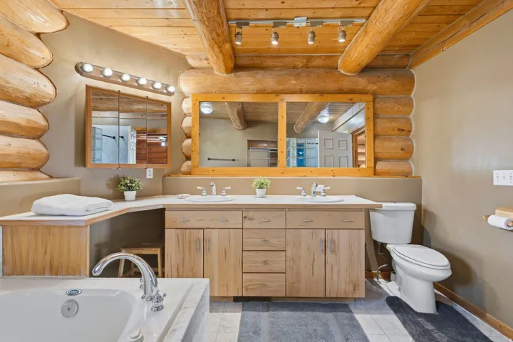 Bathroom featuring log walls, a wooden ceiling with exposed beams, double vanity, a bath, and light tile patterned flooring