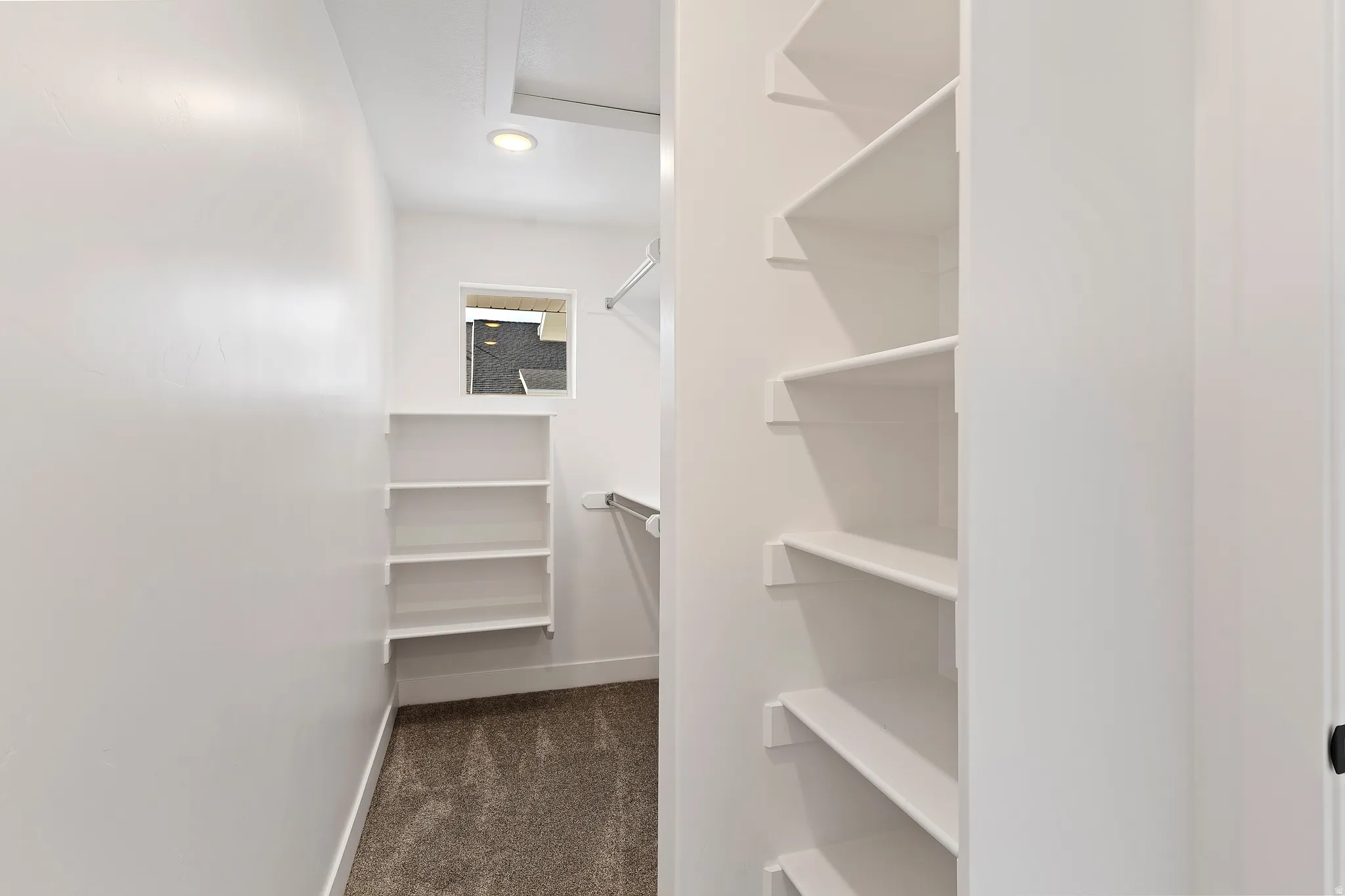 Spacious walk-in closet featuring white built-in shelving, hanging rods, and a window for natural illumination