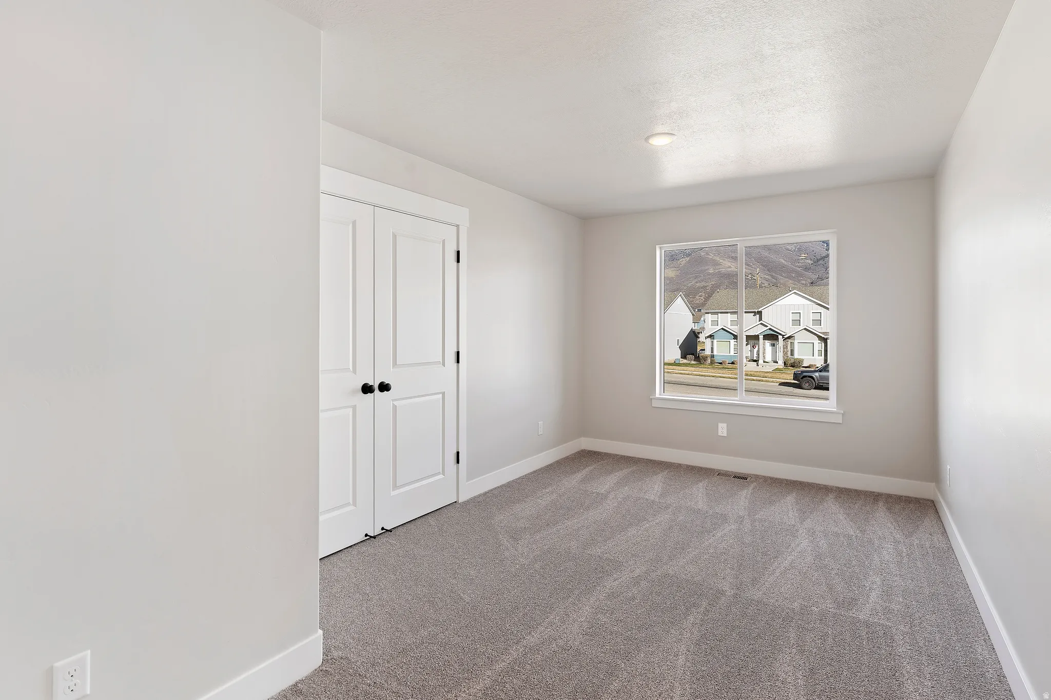 Bright room featuring neutral-toned walls, gray carpeting, a large window, and double bi-fold doors with black hardware