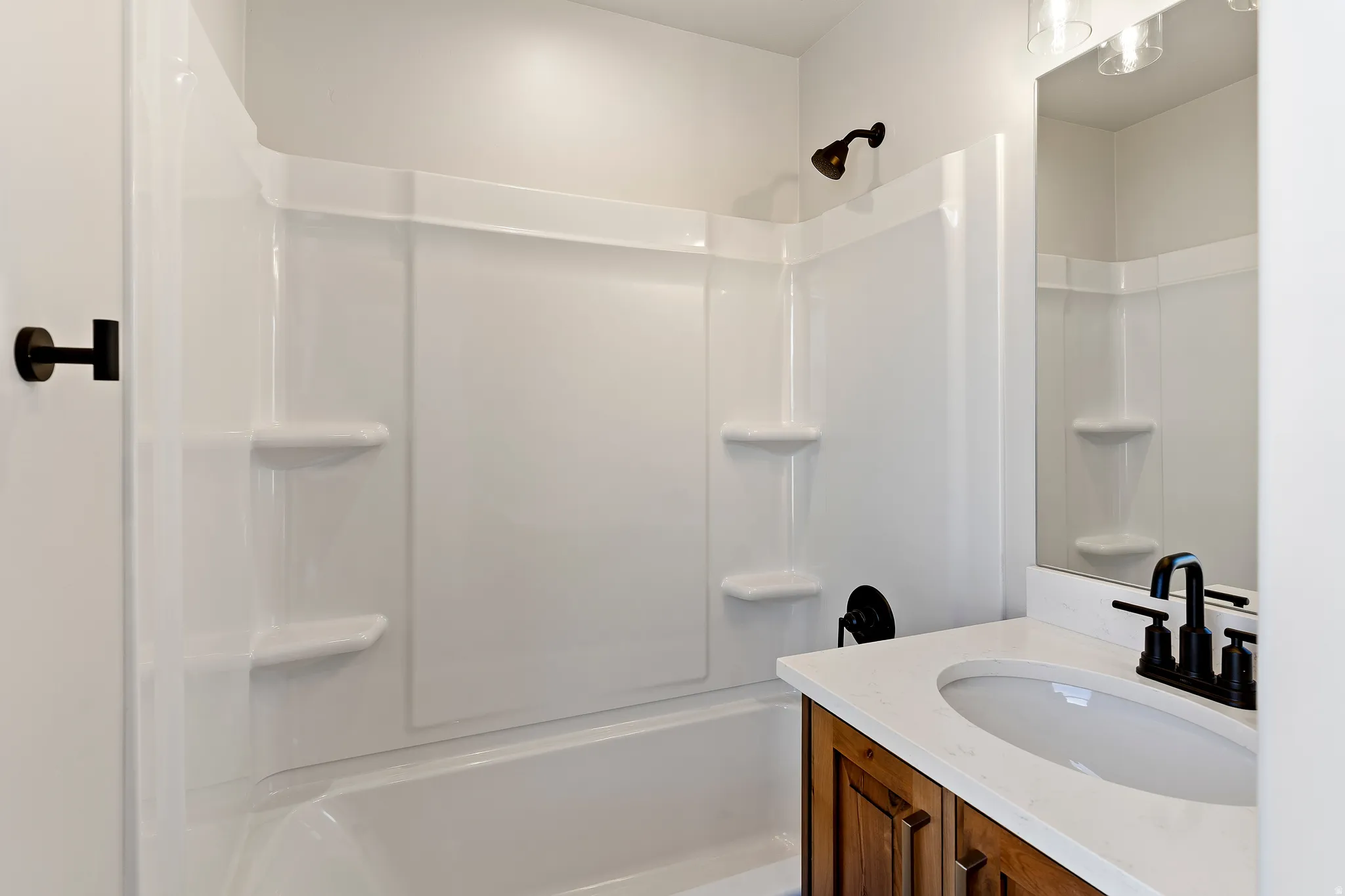 Bathroom featuring a white tub/shower combination with built-in shelving, a wood-finish vanity with panel doors, a white integrated sink, and a light-colored countertop