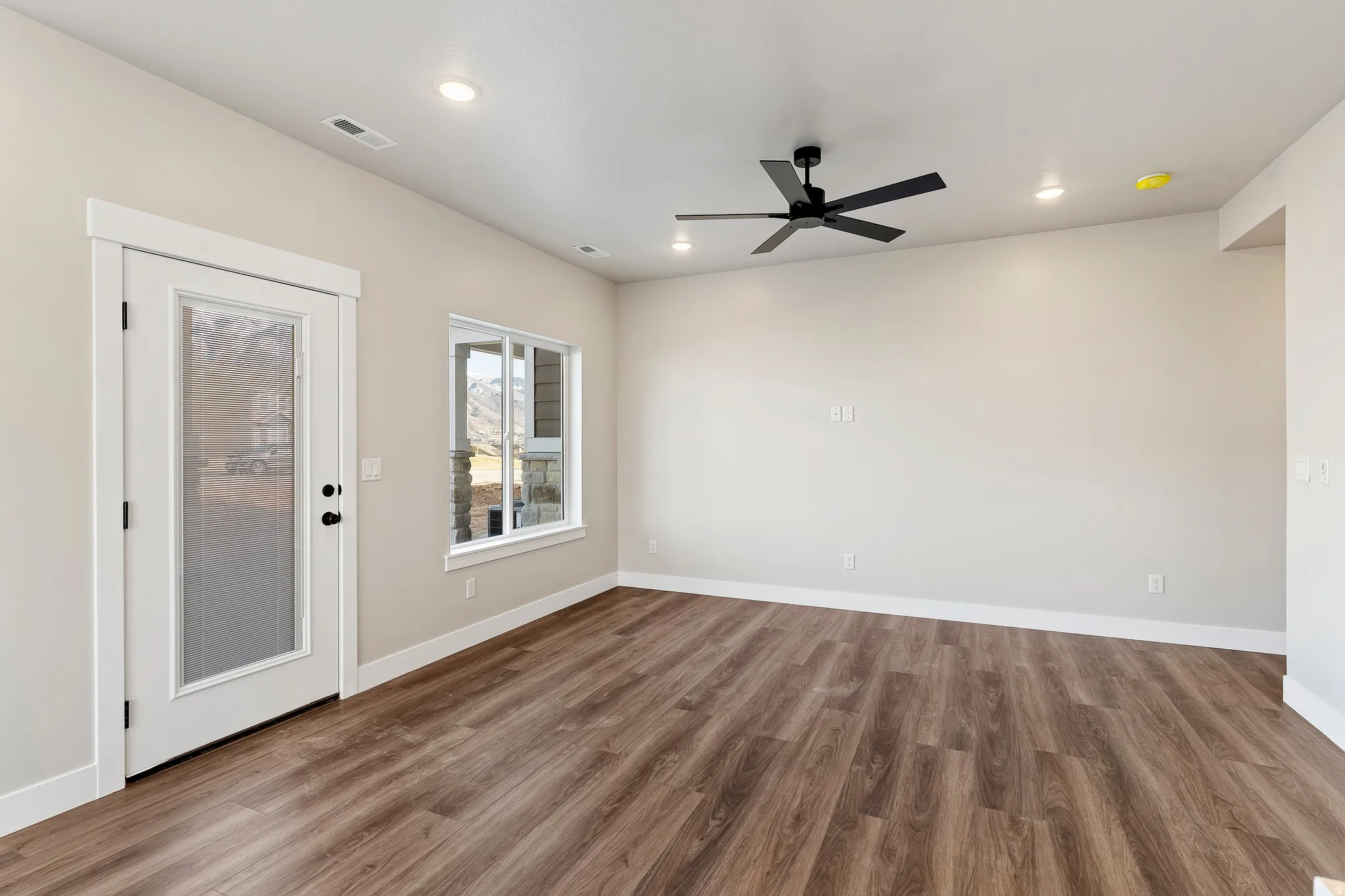 Spacious room featuring wood-finish flooring, a contemporary ceiling fan, recessed lighting, and a glass-paneled door