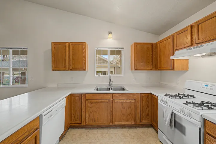 U-shaped kitchen featuring light wood cabinetry, white countertops, white appliances, and a double basin sink