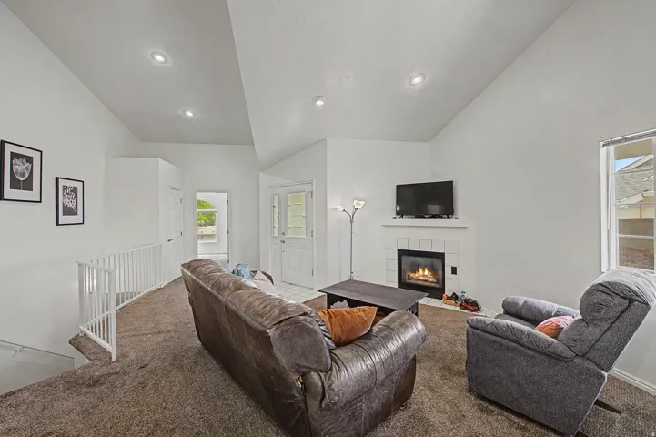 Living area featuring a white fireplace with a tile surround and mantel, vaulted ceilings, recessed lighting, and a neutral carpet