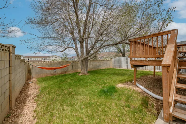 Expansive backyard featuring a mature tree, a wooden deck with railing, and a slatted privacy fence
