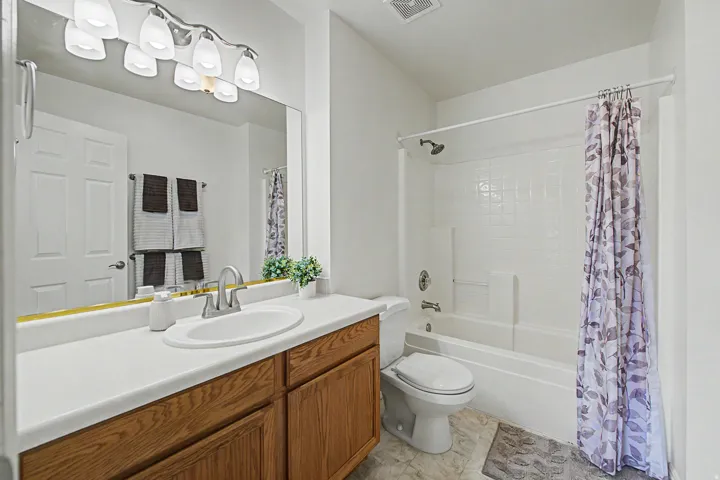 Bathroom featuring a wood-finish vanity with a white countertop and integrated sink, a large mirror, and an overhead light fixture