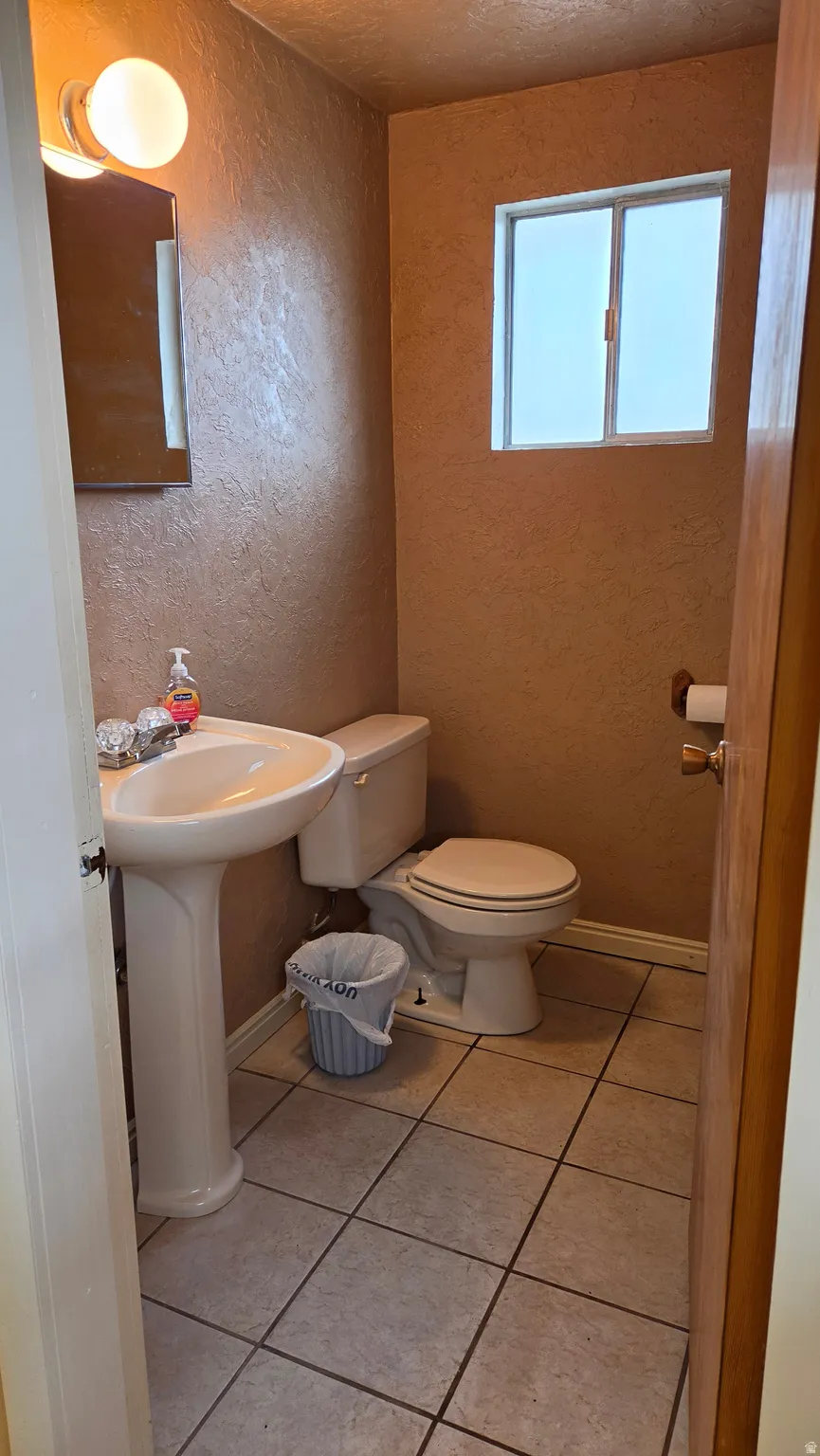 Bathroom featuring a pedestal sink, white toilet, tile flooring, and a small window for natural light