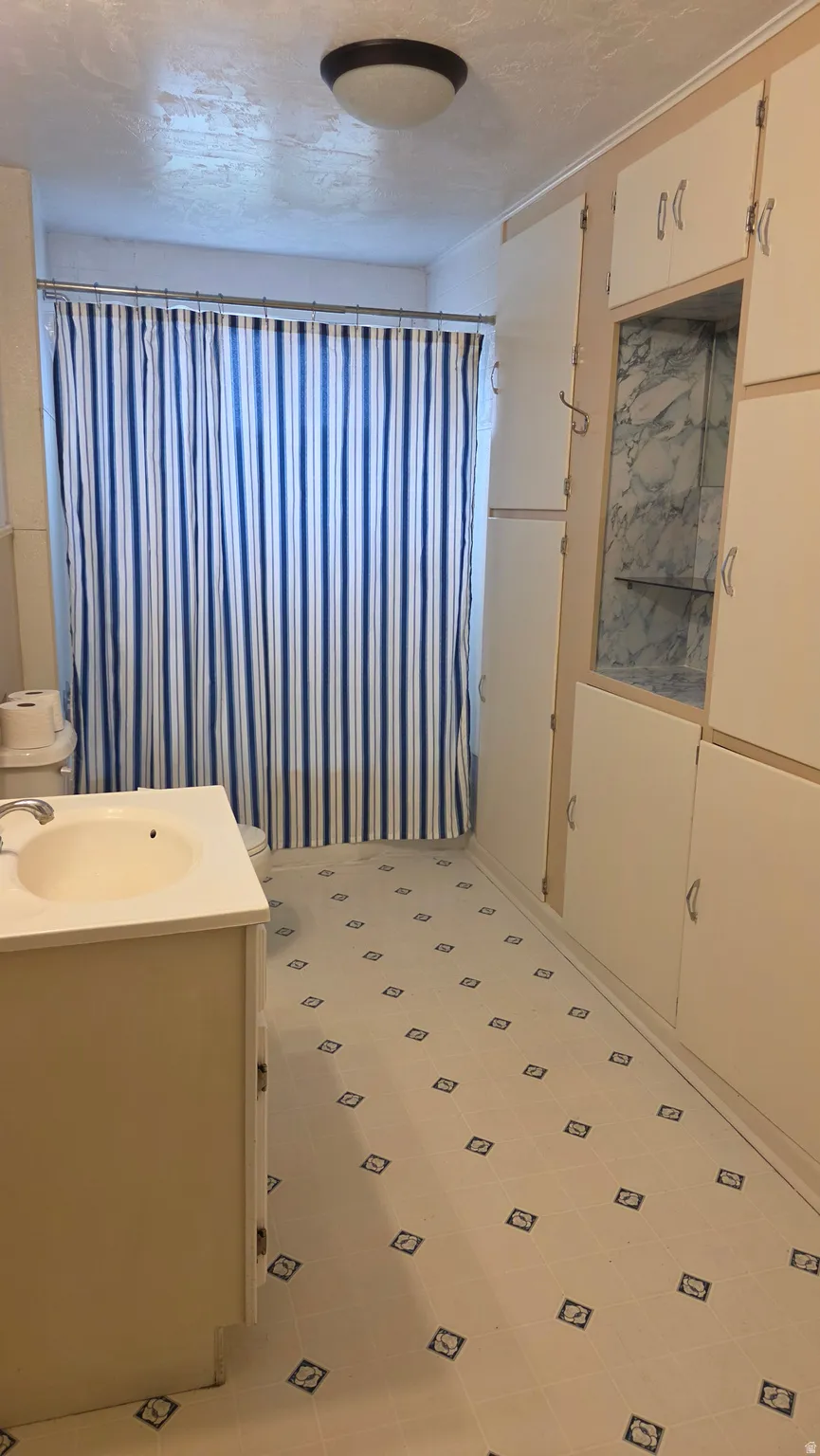 Bathroom featuring a white vanity with an integrated sink, patterned vinyl flooring, and extensive built-in cabinetry with a central display niche