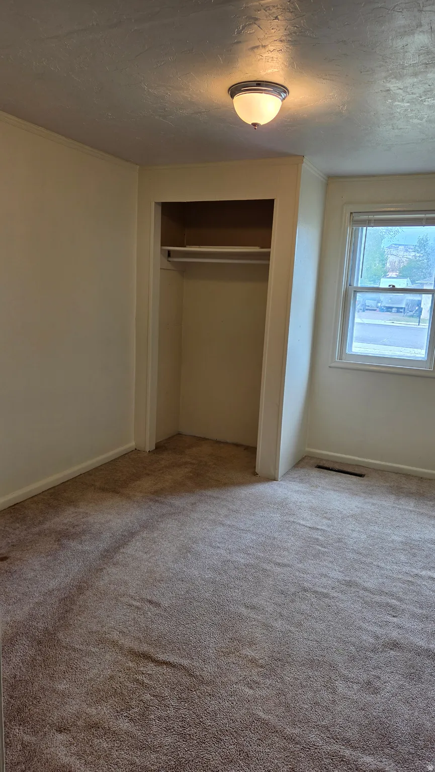 Room featuring an open closet with shelving, a window providing natural light, and a ceiling-mounted light fixture
