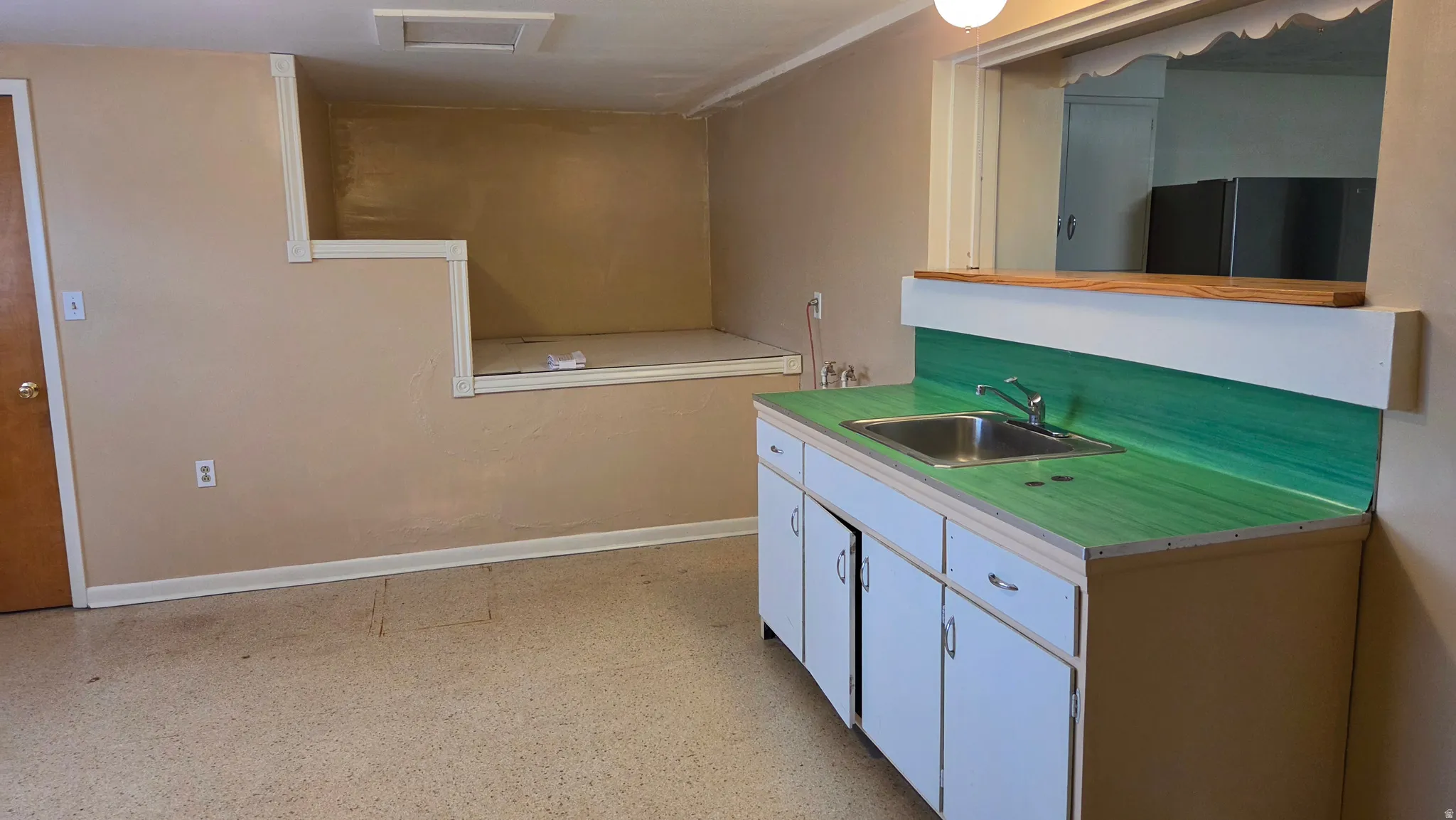 Kitchenette with a stainless steel sink, green wood-finish countertop, and white cabinetry