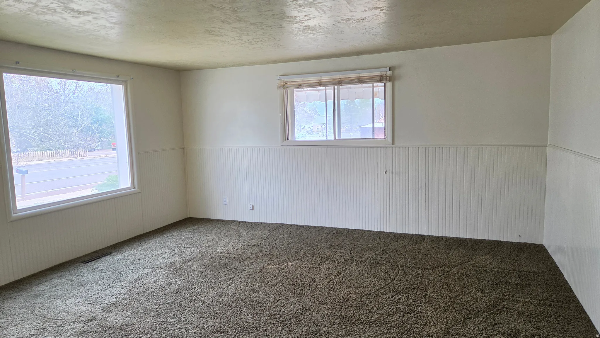 Spacious room featuring broadloom carpet, white wainscoting, and large windows