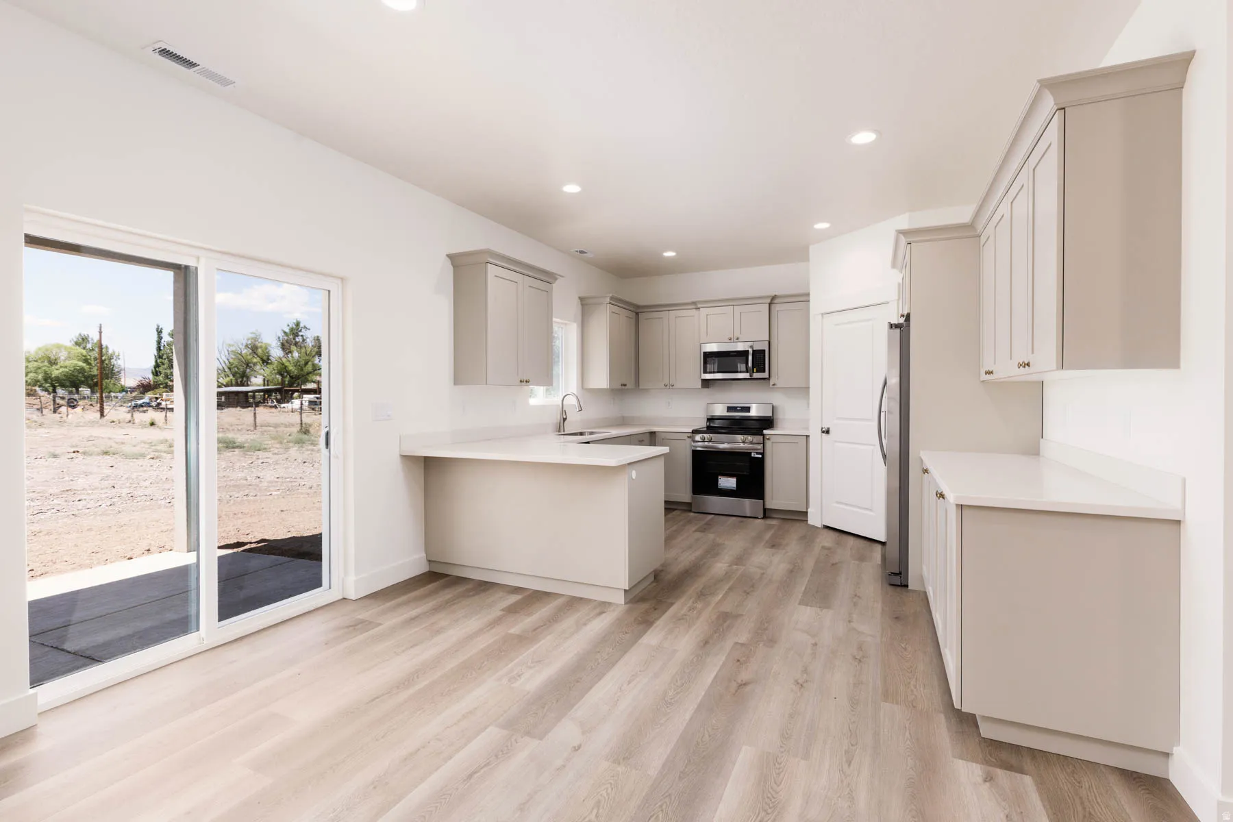Open-concept kitchen with light wood-finish flooring, recessed lighting, white countertops, and light gray cabinetry