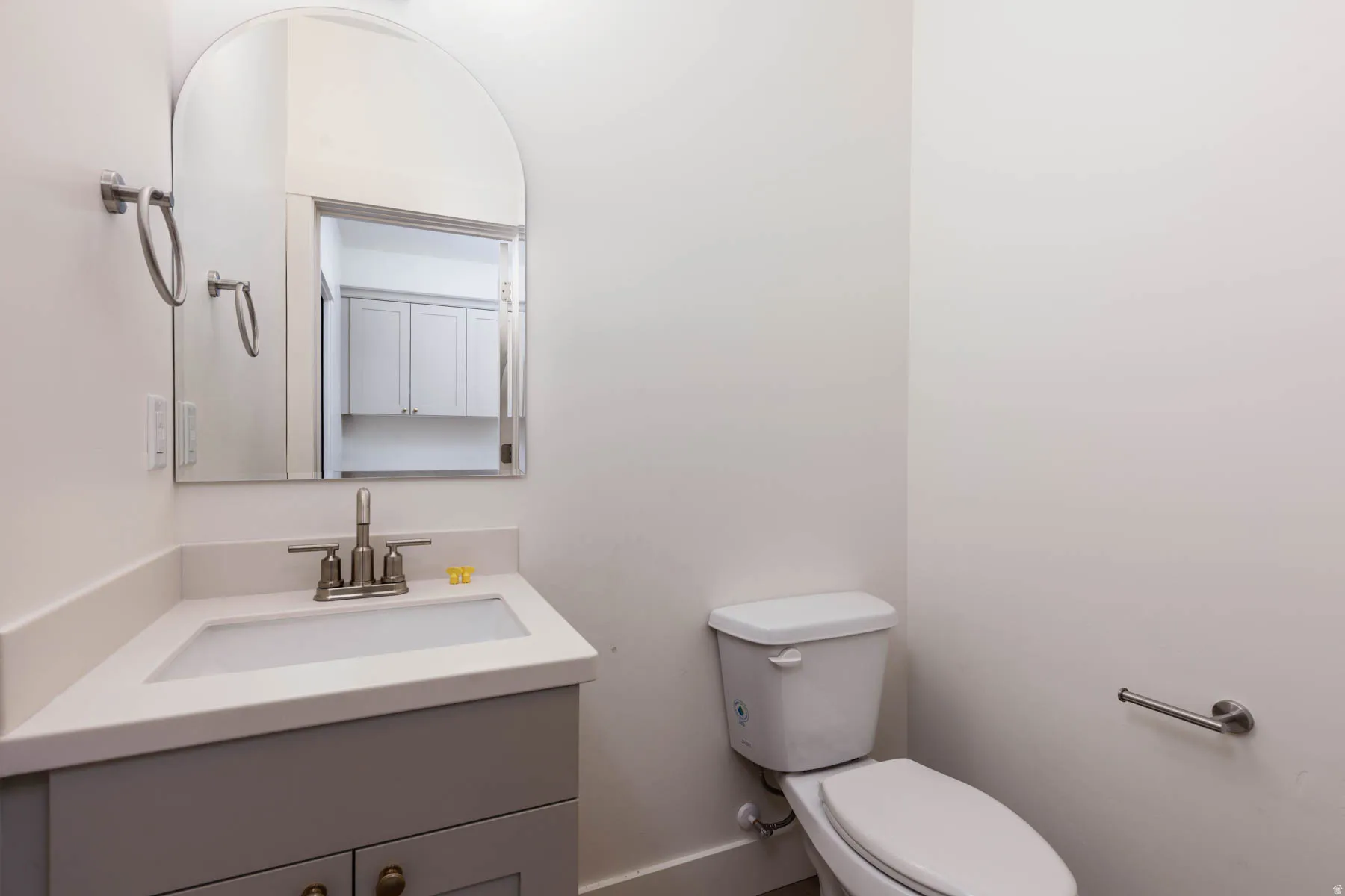 Bathroom featuring a corner vanity with a white countertop and integrated sink, a brushed nickel faucet, and a wall-mounted arched mirror