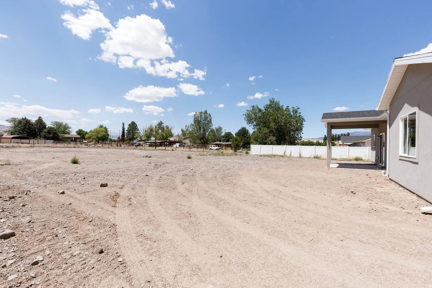 Expansive, undeveloped lot with a partially visible exterior wall, covered patio, and a white perimeter fence