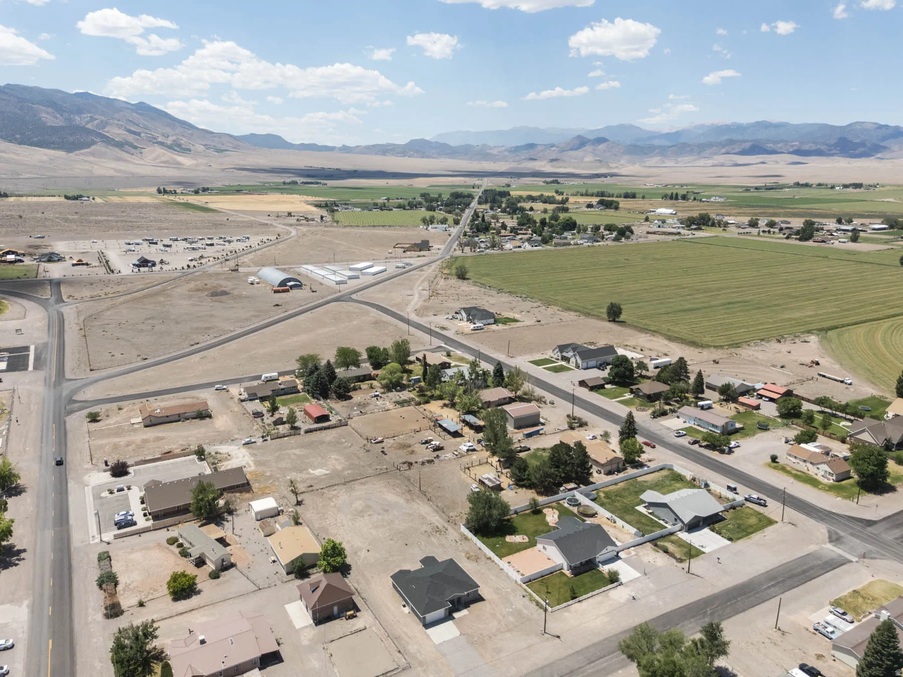 Expansive aerial perspective showcasing a neighborhood with varied residential properties, agricultural fields, and mountainous terrain in the distance