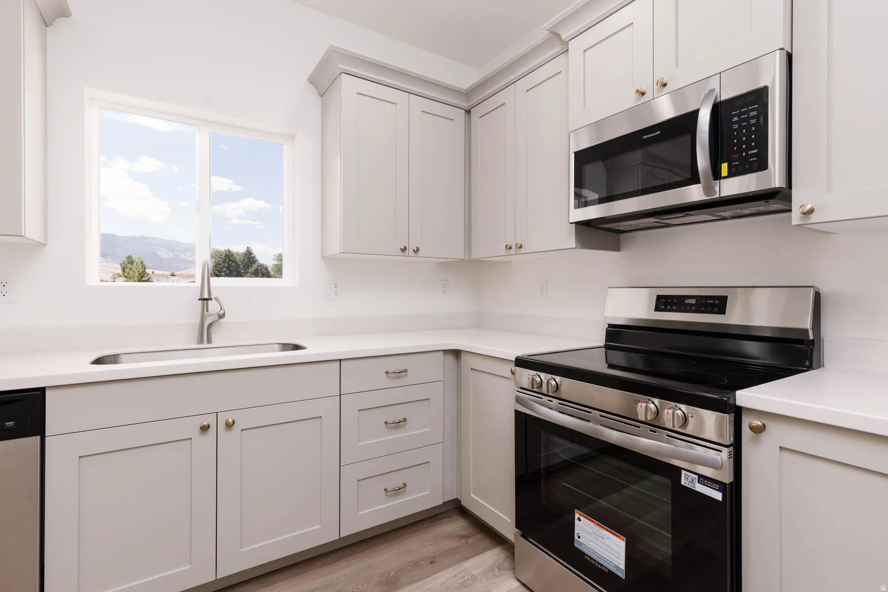 Modern kitchen featuring light gray cabinetry, stainless steel appliances, a window above the sink, light-toned countertops, and wood-finish flooring