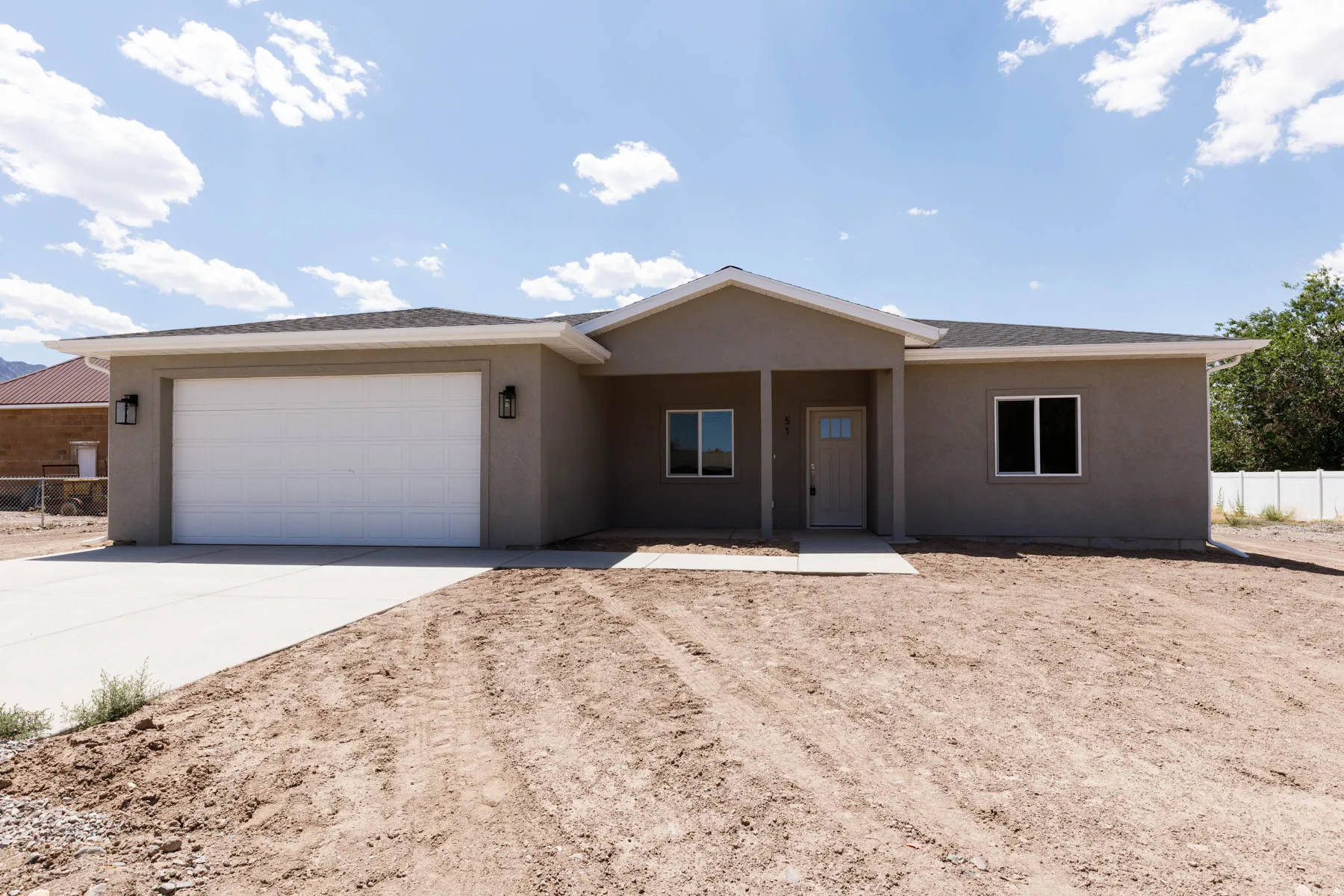 Contemporary single-story residence featuring a two-car garage with a white panel door, stucco exterior finish, and a covered entryway