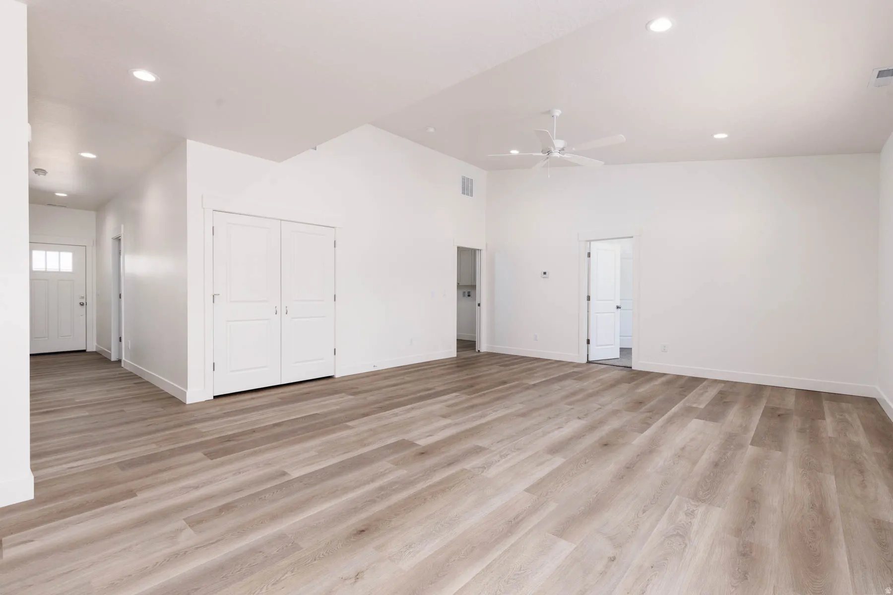 Spacious room featuring wood-finish flooring, white walls, vaulted ceilings, recessed lighting, and a ceiling fan
