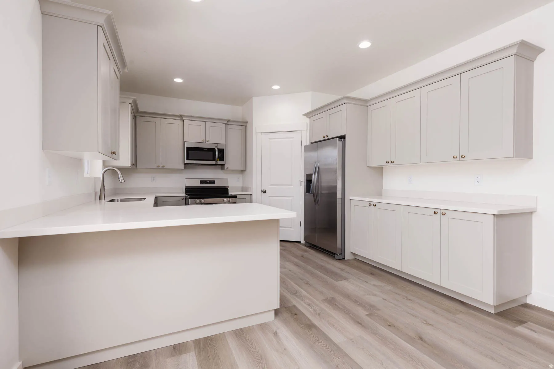 Modern kitchen featuring light gray cabinetry, white countertops, stainless steel appliances, wood-finish flooring, and recessed lighting