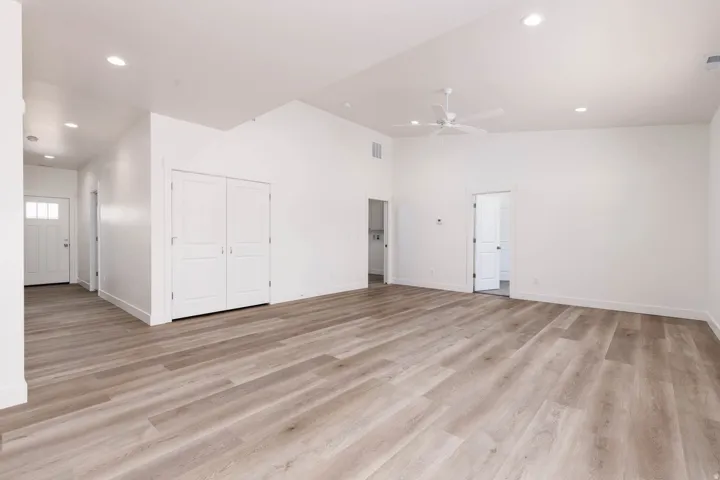Spacious room featuring wood-finish flooring, white walls, vaulted ceilings, recessed lighting, and a ceiling fan