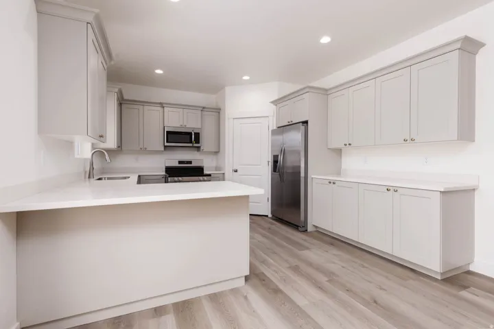 Modern kitchen featuring light gray cabinetry, white countertops, stainless steel appliances, wood-finish flooring, and recessed lighting