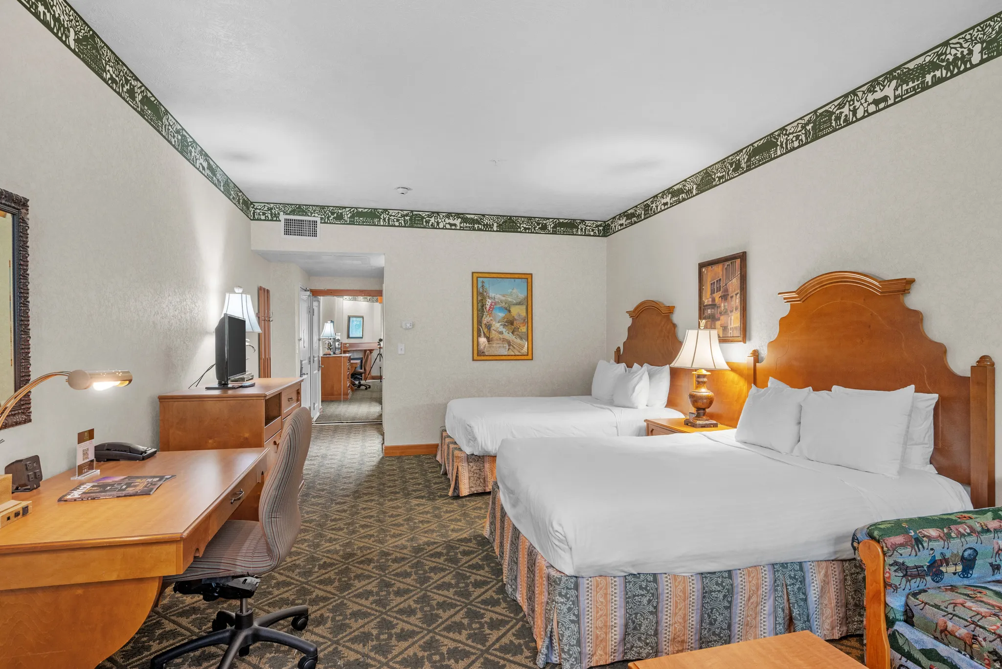Bedroom featuring two beds with wood headboards, textured walls with decorative border, patterned carpet flooring, and a dedicated workspace with a desk and chair