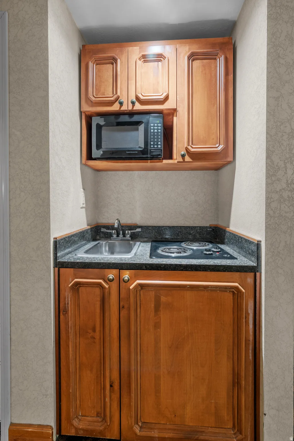 Compact kitchenette featuring wood cabinetry, a built-in microwave, a stainless steel sink, and a two-burner cooktop