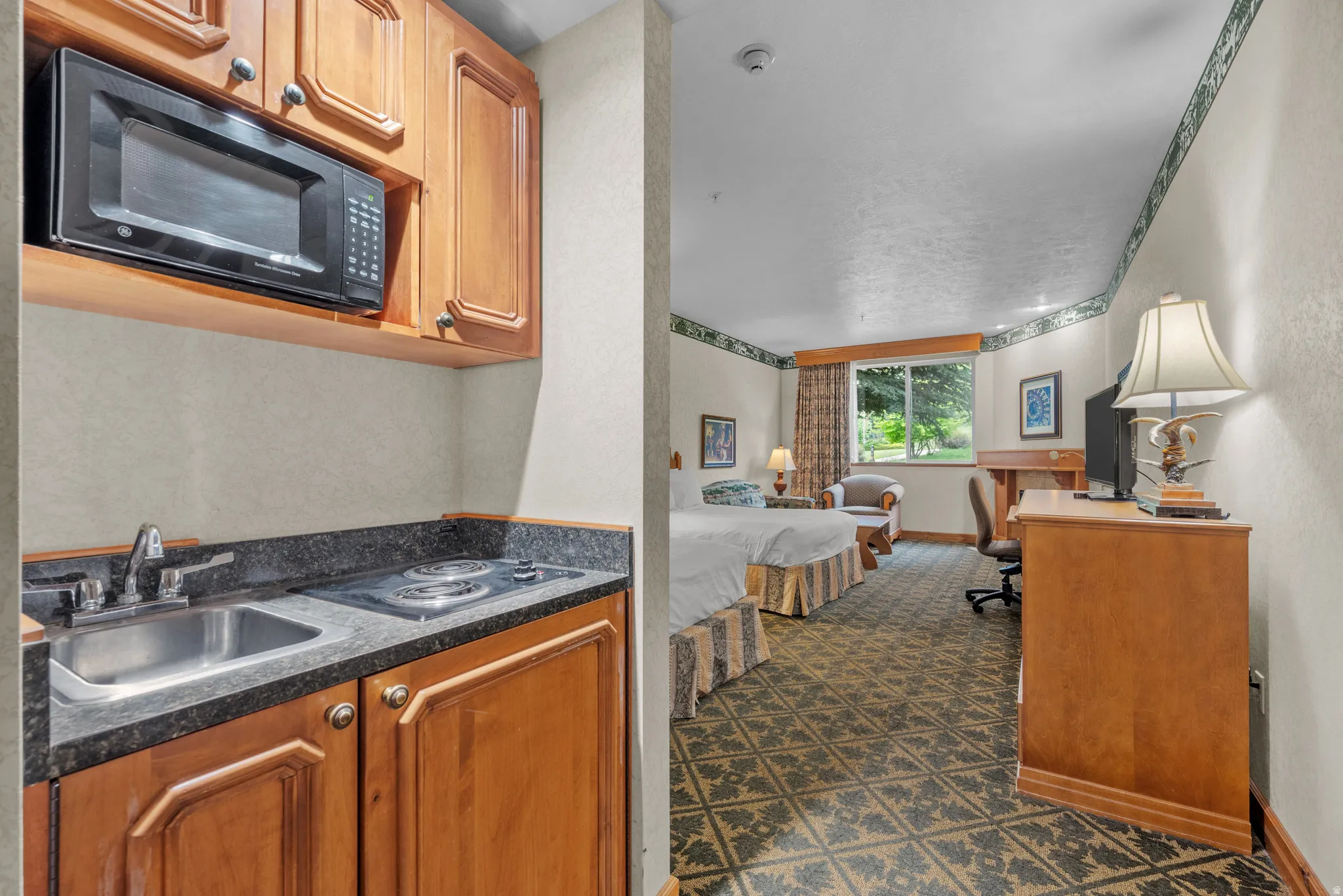 Compact kitchenette featuring wood cabinetry, dark stone-finish countertops, stainless steel sink, two-burner cooktop, and an integrated microwave