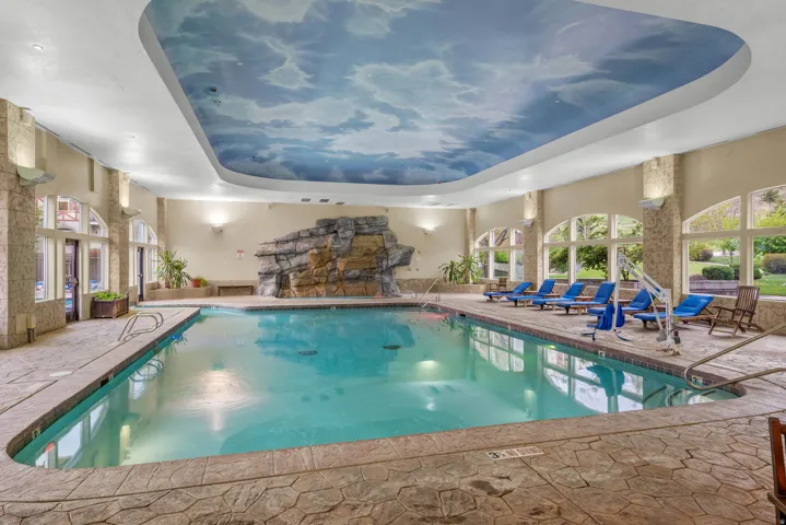 Indoor swimming pool featuring a decorative rock waterfall, a cloud-mural ceiling, and arched windows