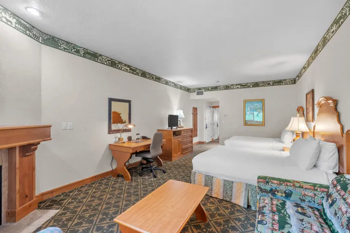 Spacious room featuring patterned carpeting, two beds, a desk area, and a wood mantelpiece
