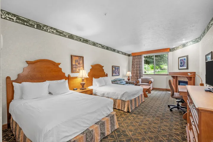 Spacious interior featuring two wood-finish headboards, patterned carpeting, a large window, a built-in electric fireplace, and a dedicated desk area