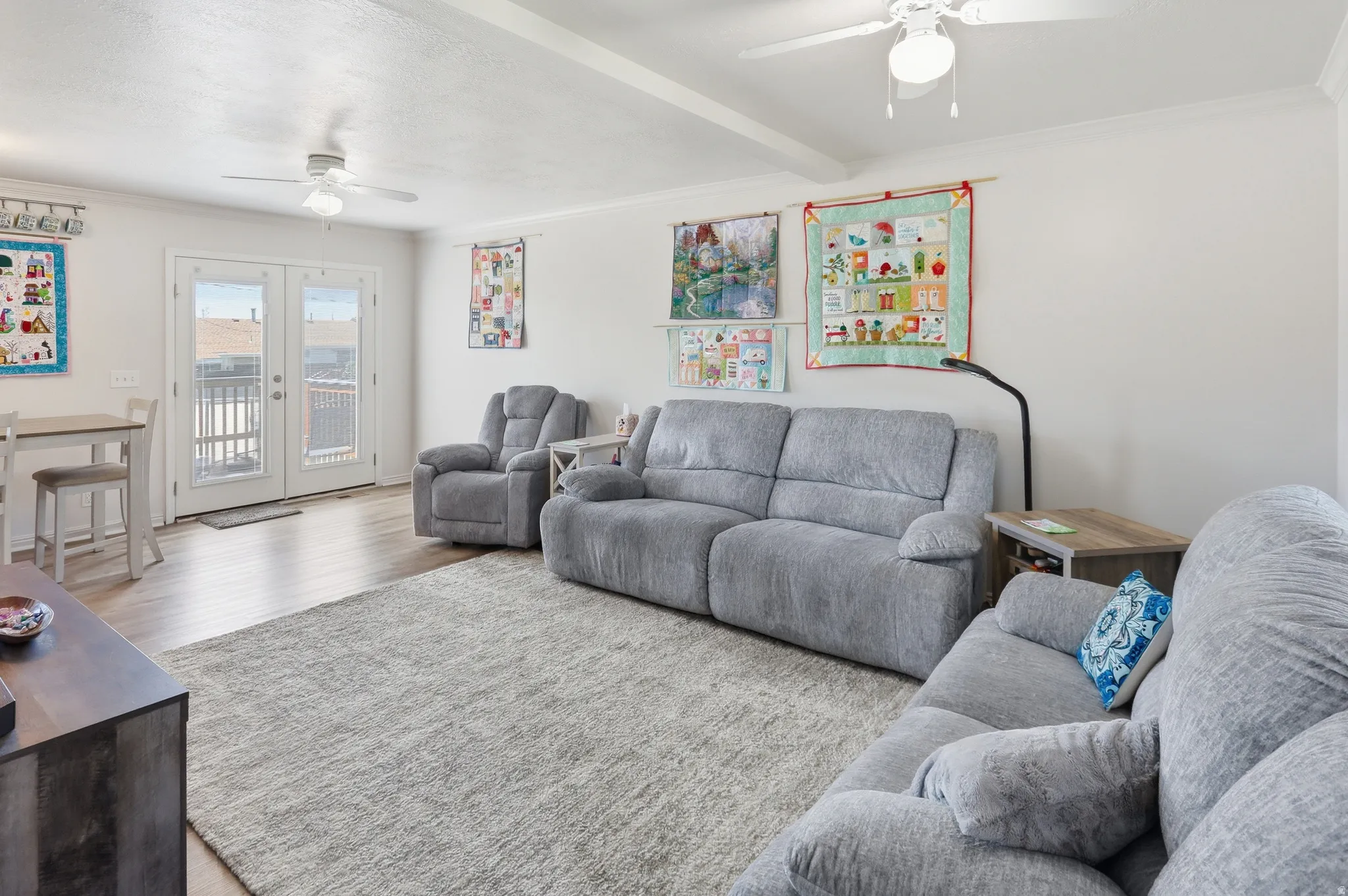 Spacious living area featuring wood-finish flooring, two ceiling fans with integrated lighting, and crown molding