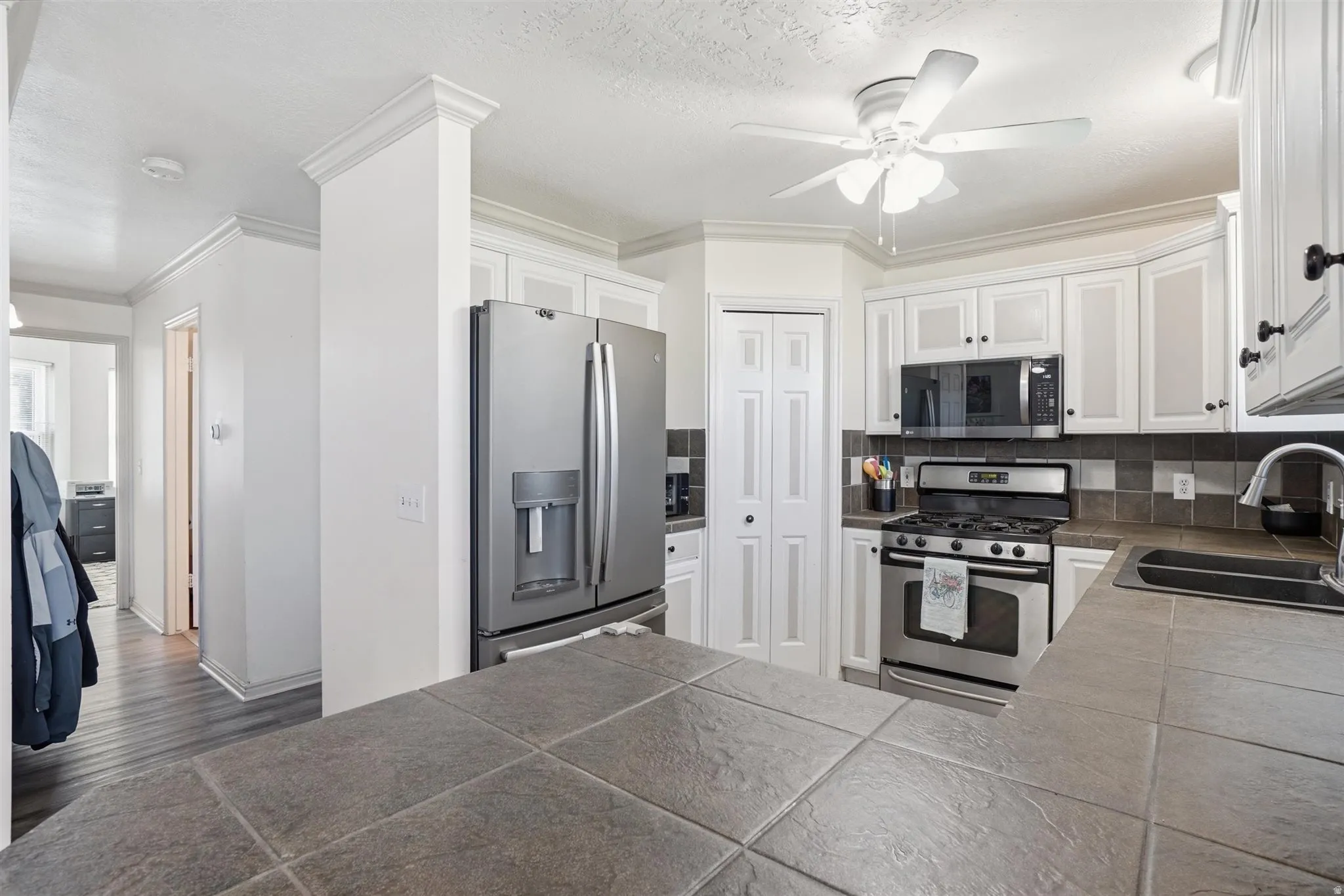 Well-appointed kitchen featuring white cabinetry, stainless steel appliances, a tile backsplash, and a ceiling fan