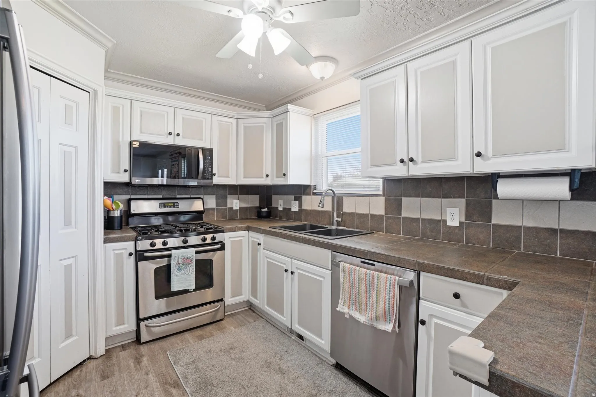 Kitchen featuring white cabinetry, stainless steel appliances, a double basin sink, and wood-finish flooring